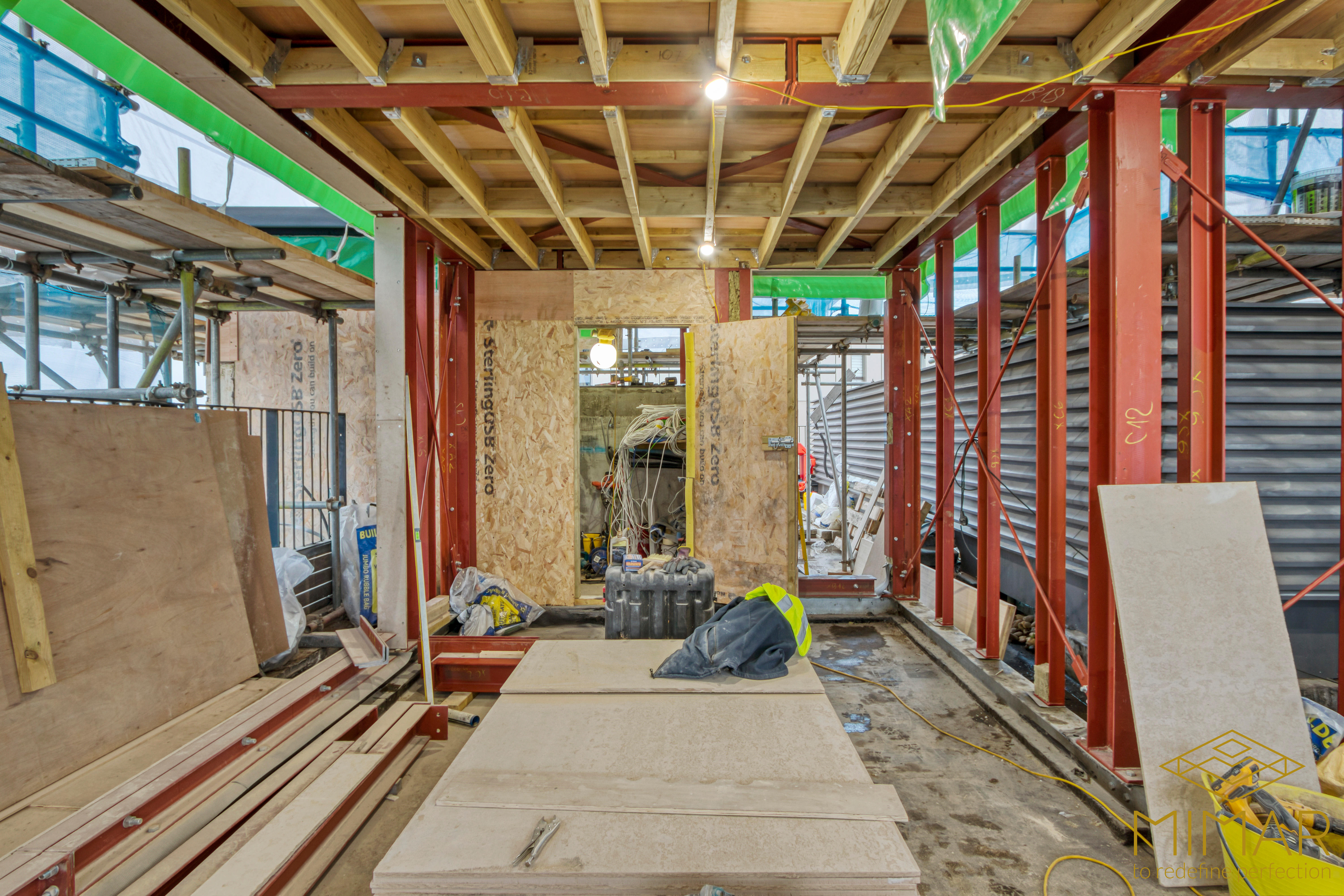 The image shows a construction site with exposed wooden beams, steel supports, and construction materials, indicating an ongoing basement construction project.