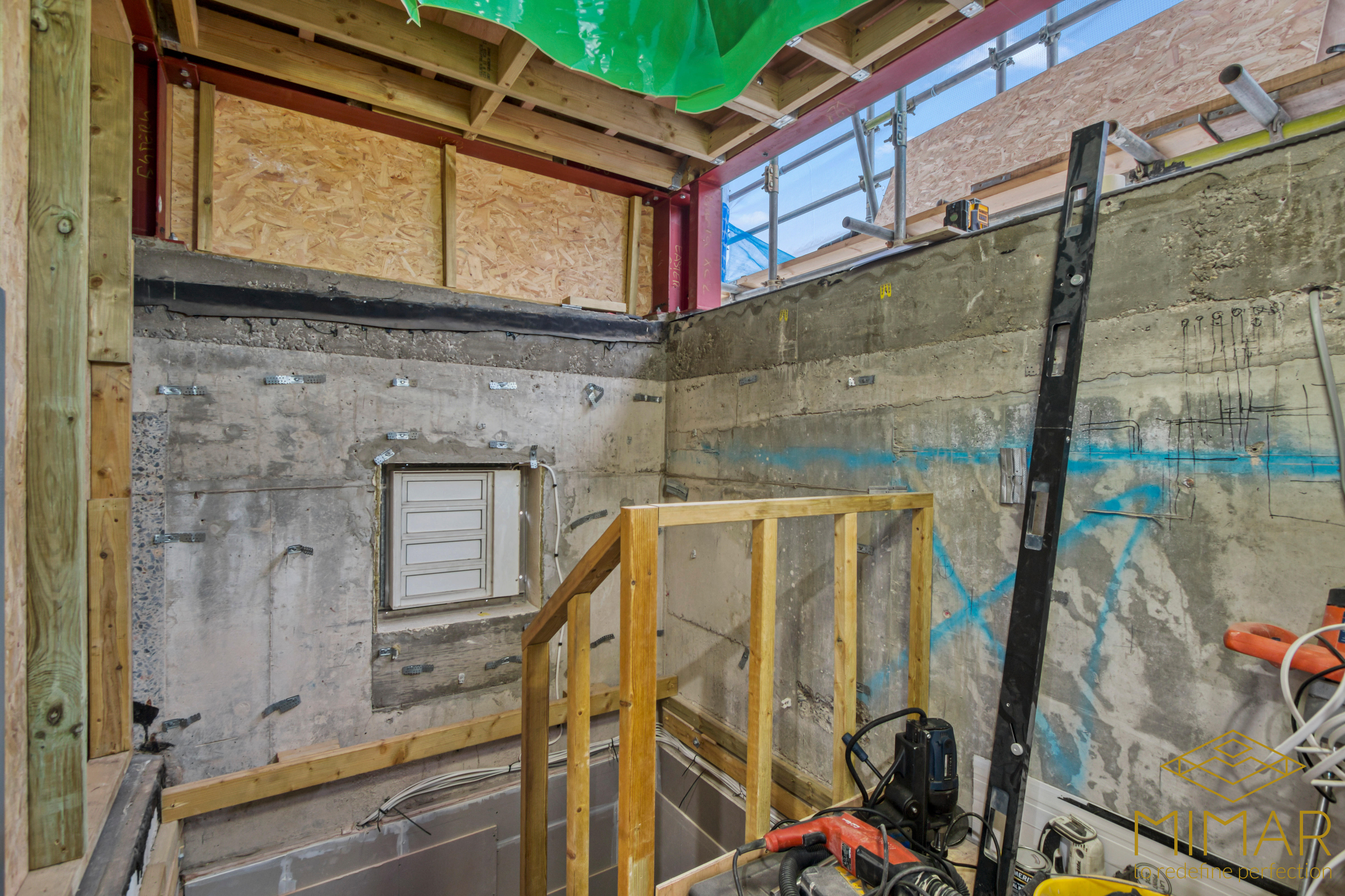 Interior view of a partially constructed basement with exposed concrete walls, wooden frameworks, and construction tools.