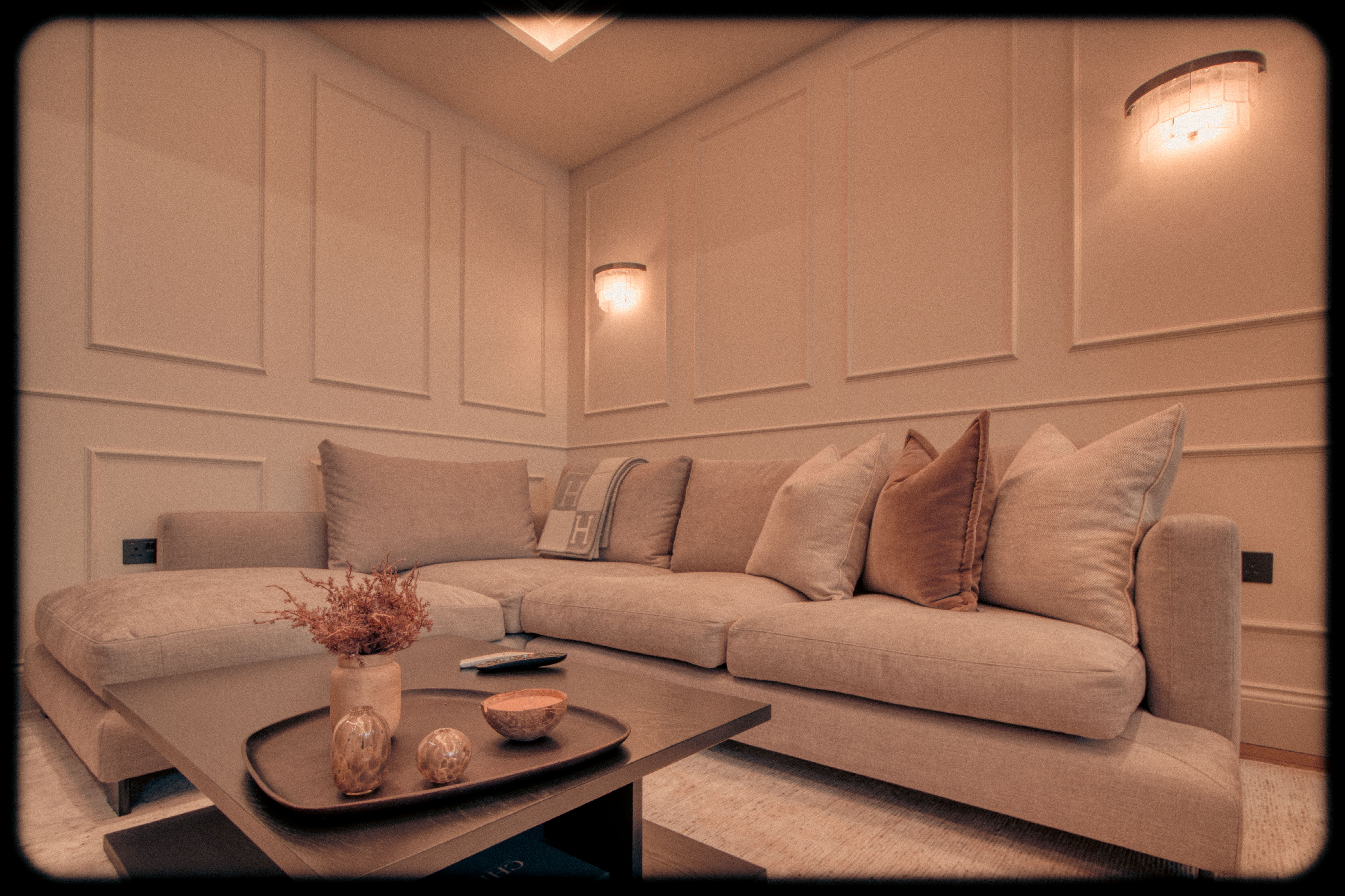 Modern basement living room with beige sectional sofa, panelled walls, and ambient lighting.