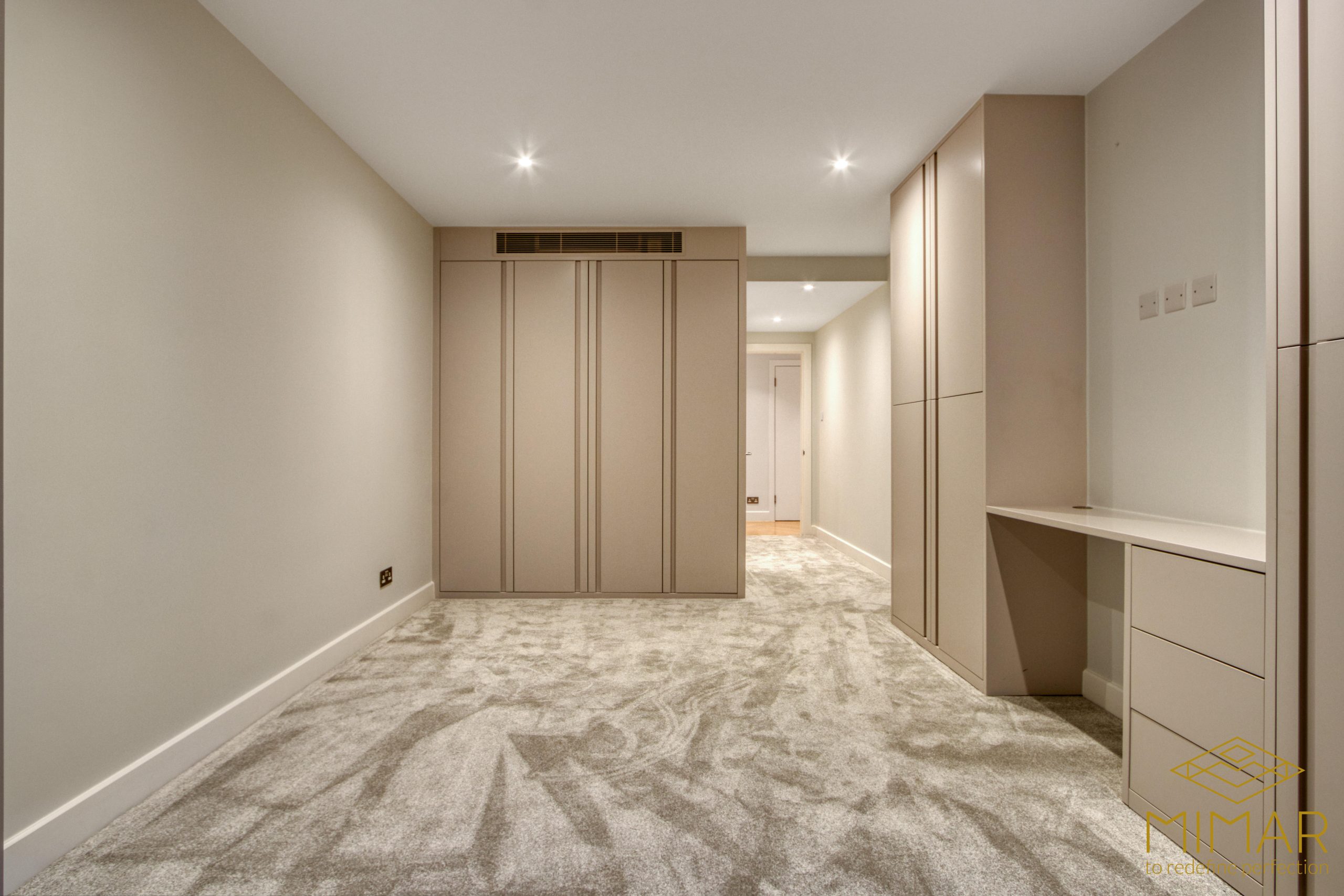A newly refurbished basement room featuring built-in storage cabinets, a desk area, and recessed lighting with carpet flooring.