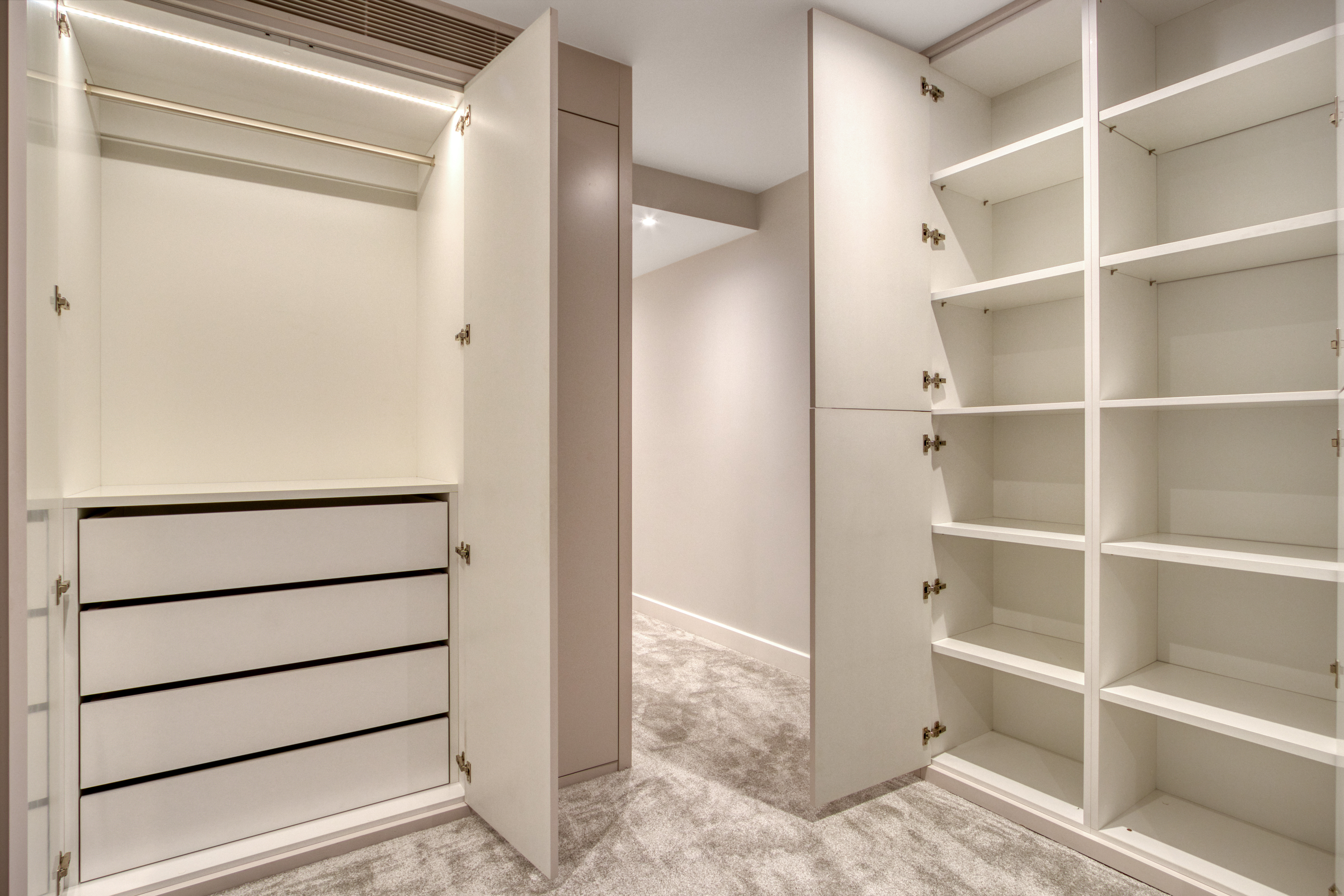 A spacious, custom-built wardrobe with open shelves and closed drawers, featuring interior lighting and a modern design.