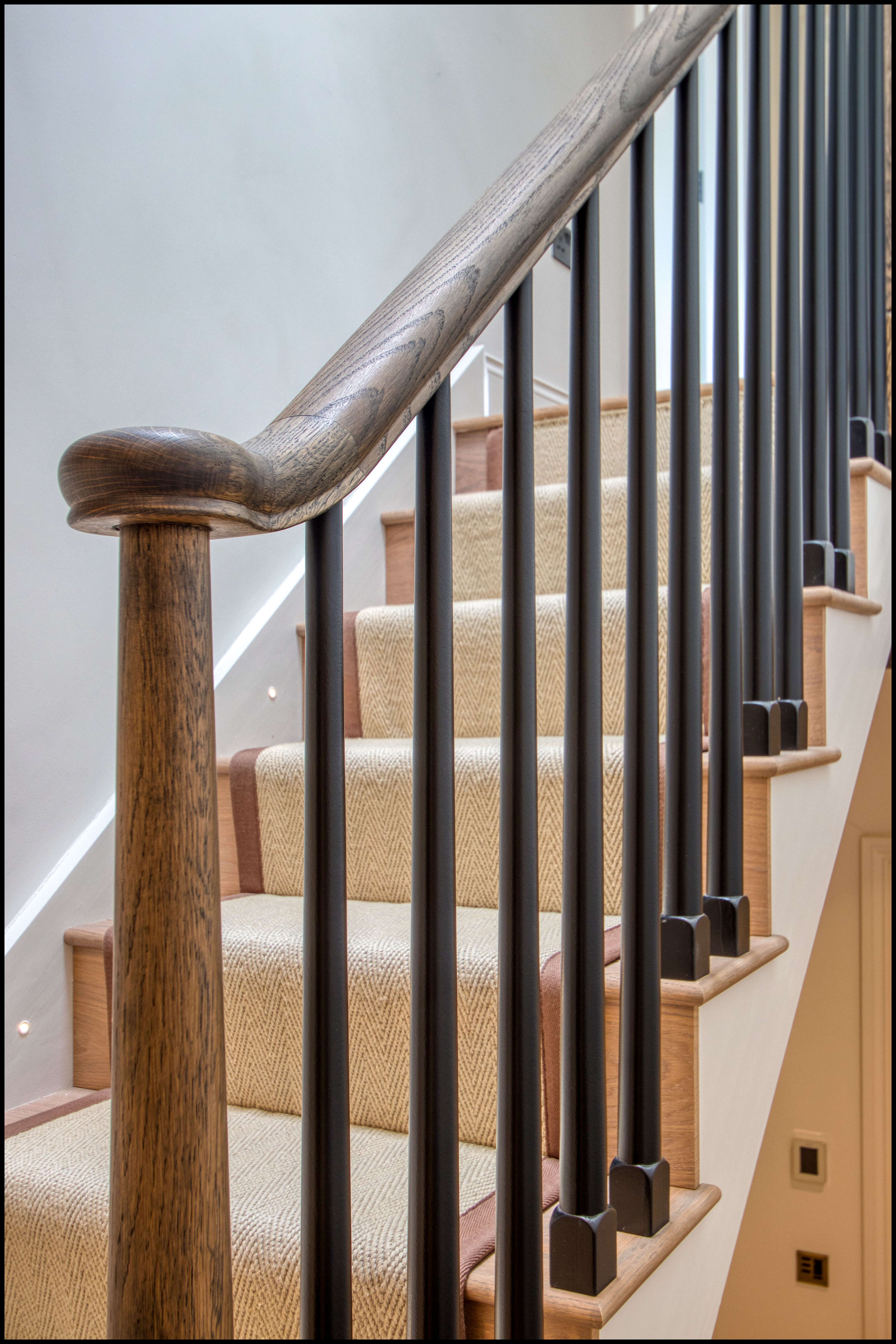 A custom wooden staircase with metal balusters and a carpet runner on each step.