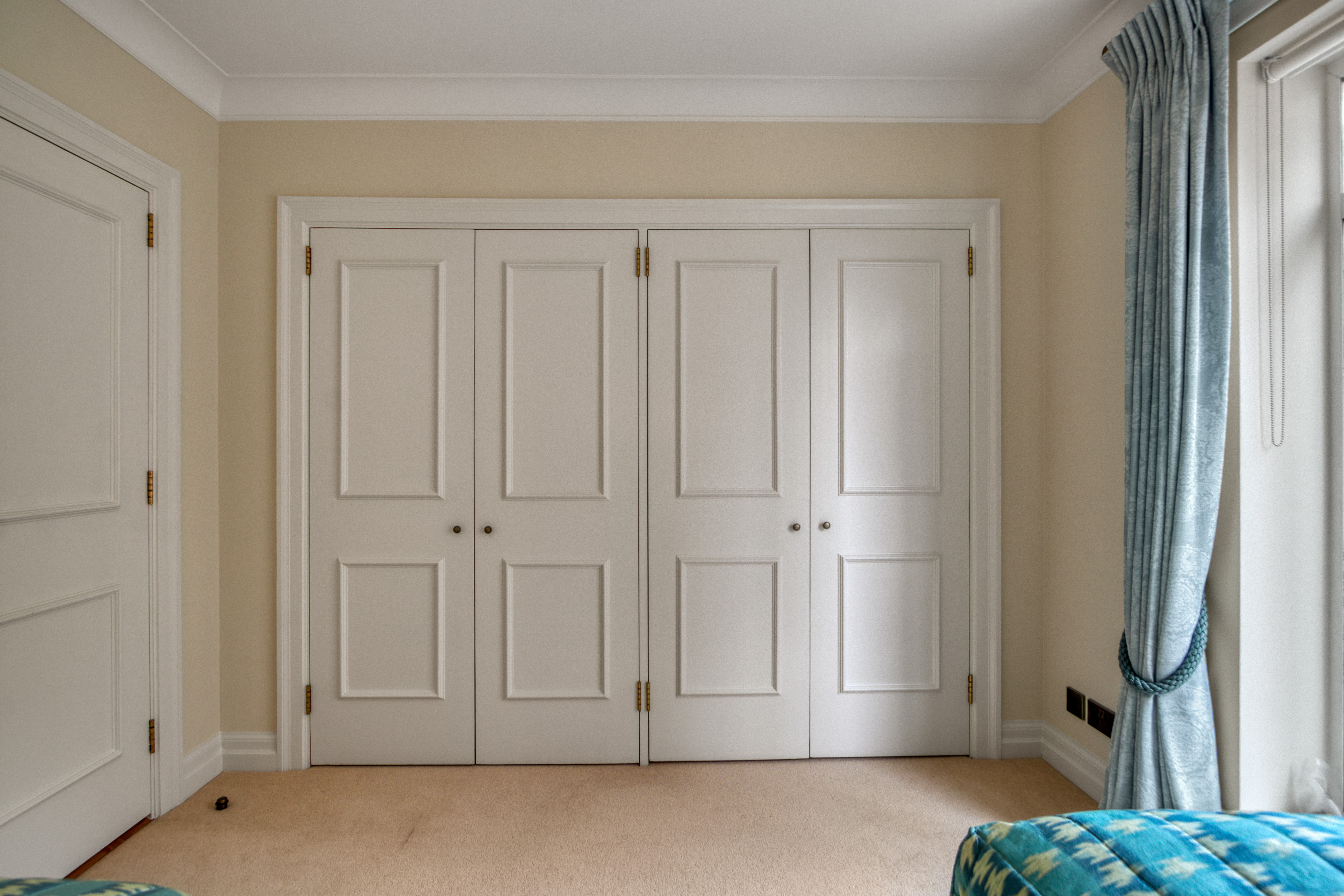 Image of a room with white custom-built wardrobe doors, beige walls, and blue curtains.