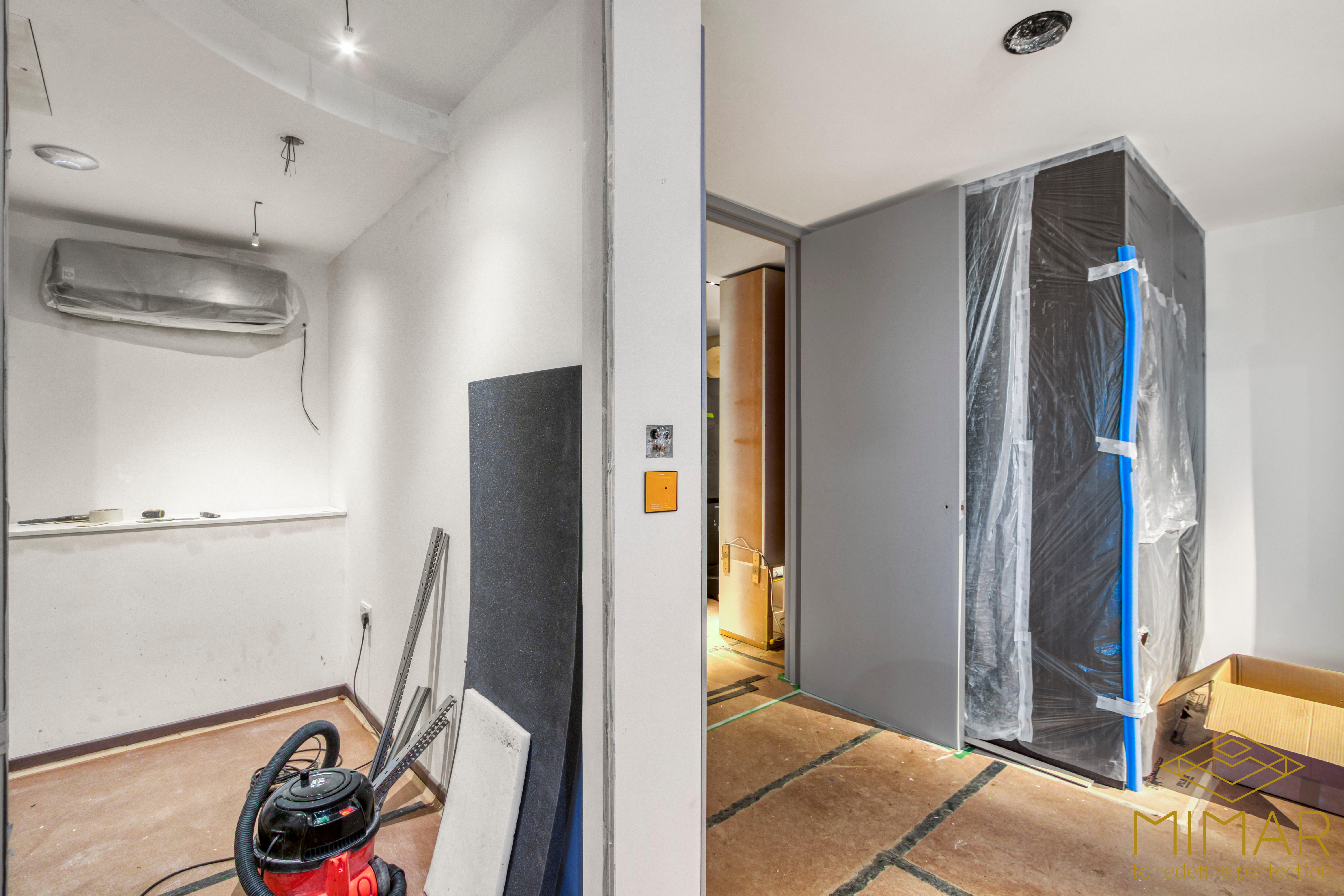 Room under renovation with drywall, light fixtures, and a covered HVAC unit, indicating ongoing refurbishment work.