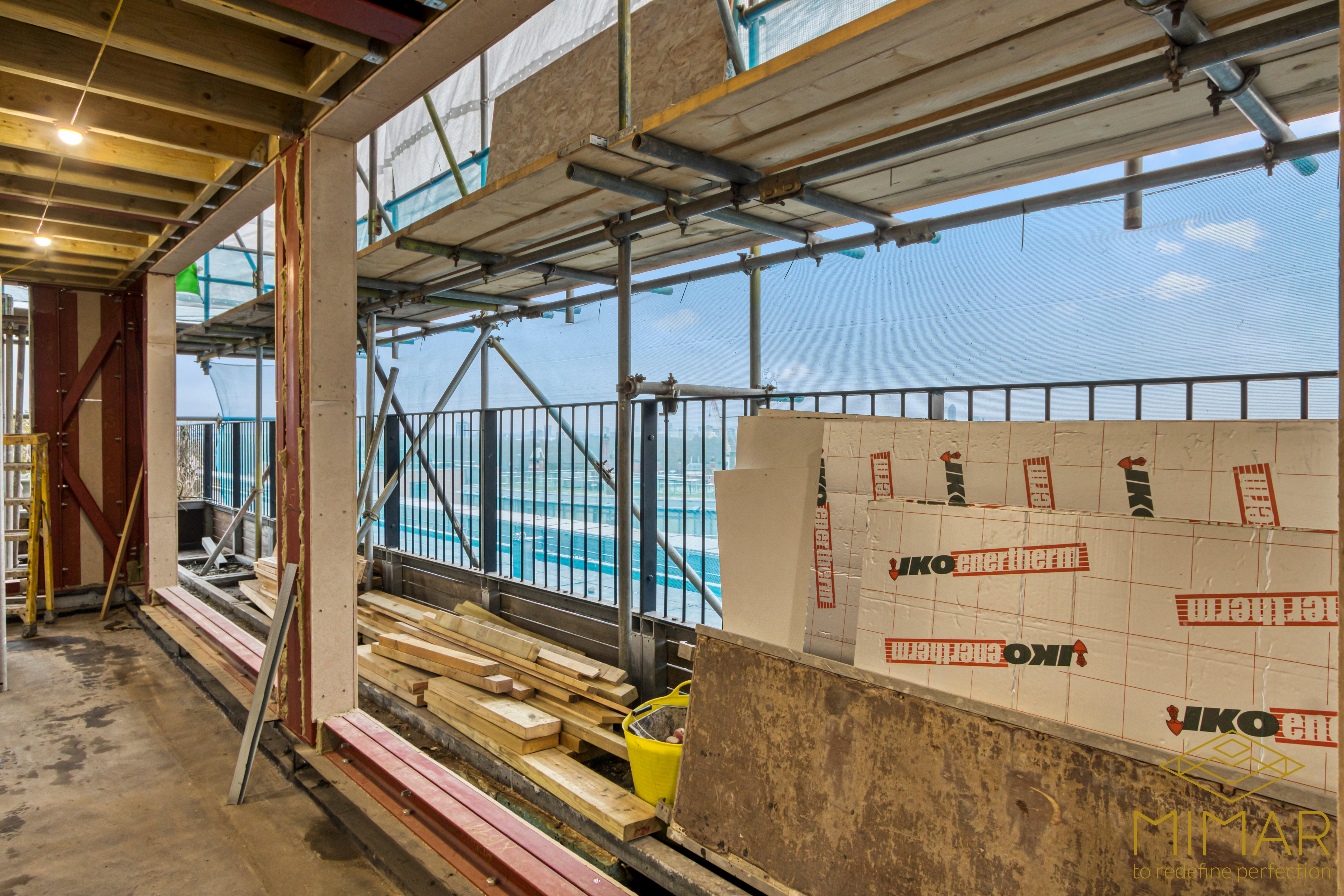 An in-progress construction site showing structural framing, insulating materials, and scaffolding for a house extension.