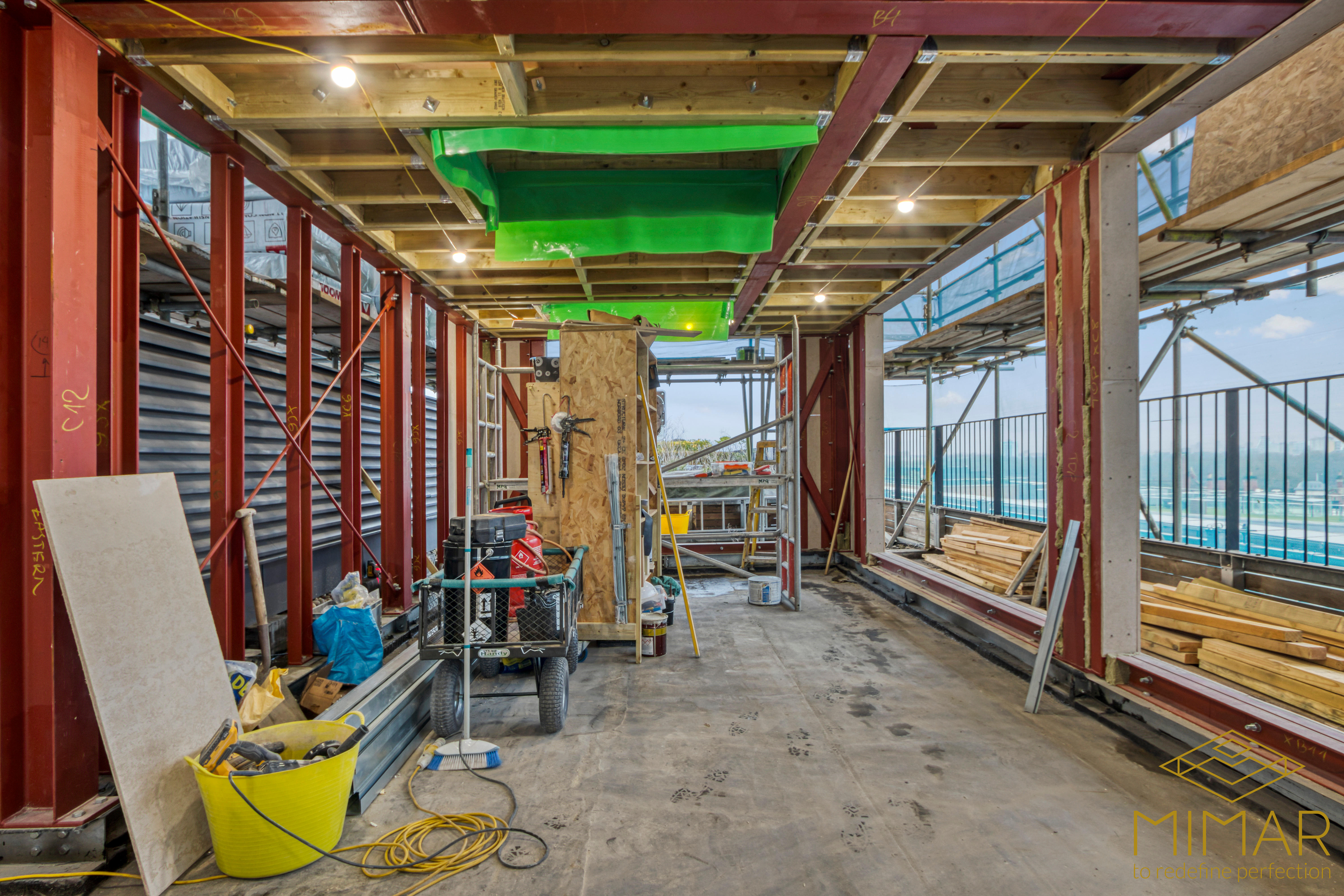Interior view of a house extension under construction with exposed beams, steel supports, and building materials.