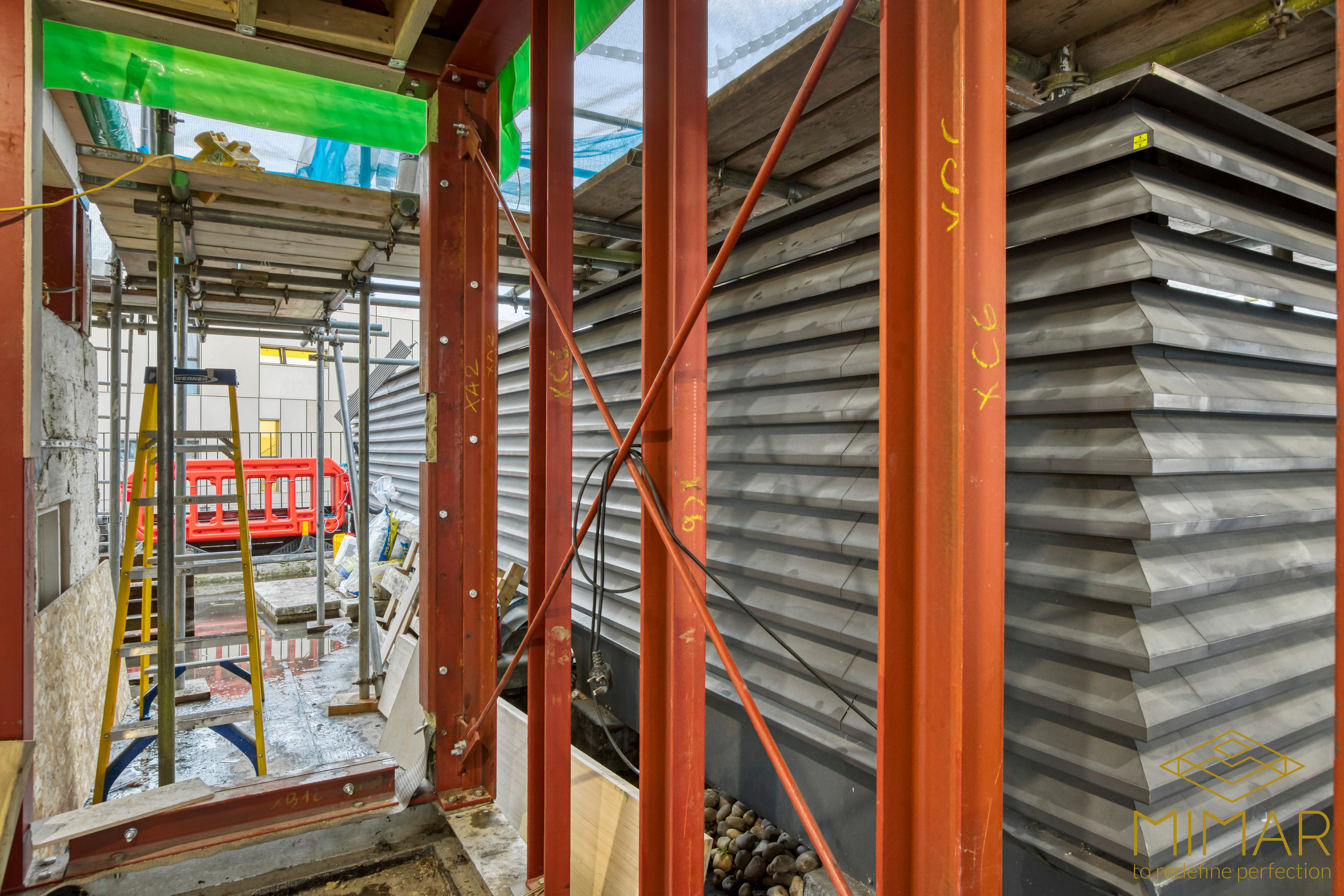 Steel frame construction for a house extension with scaffolding and insulated metal cladding.