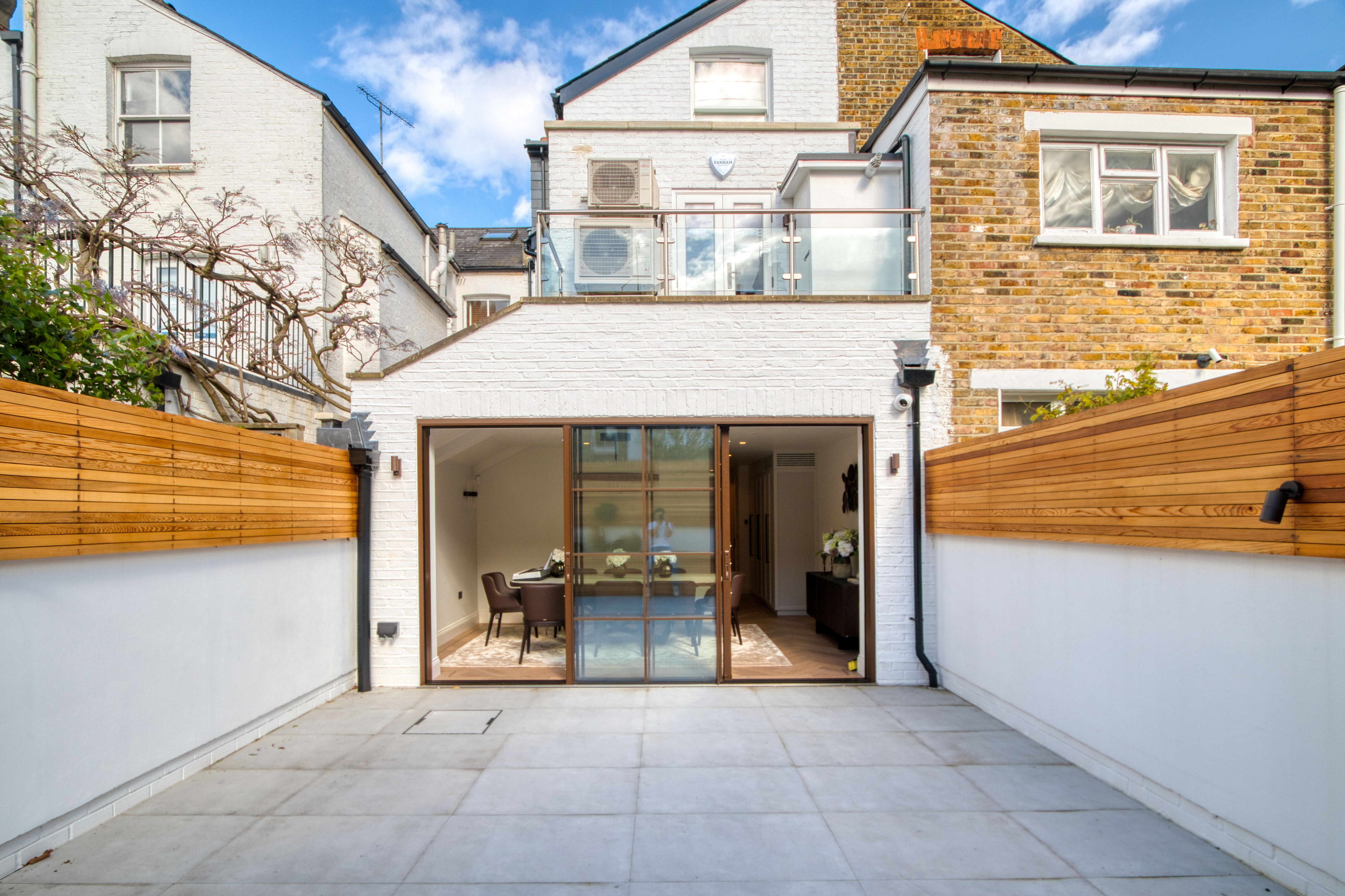 Modern house extension with a glass door opening to a tidy backyard space, featuring wooden fencing and outdoor tiles.