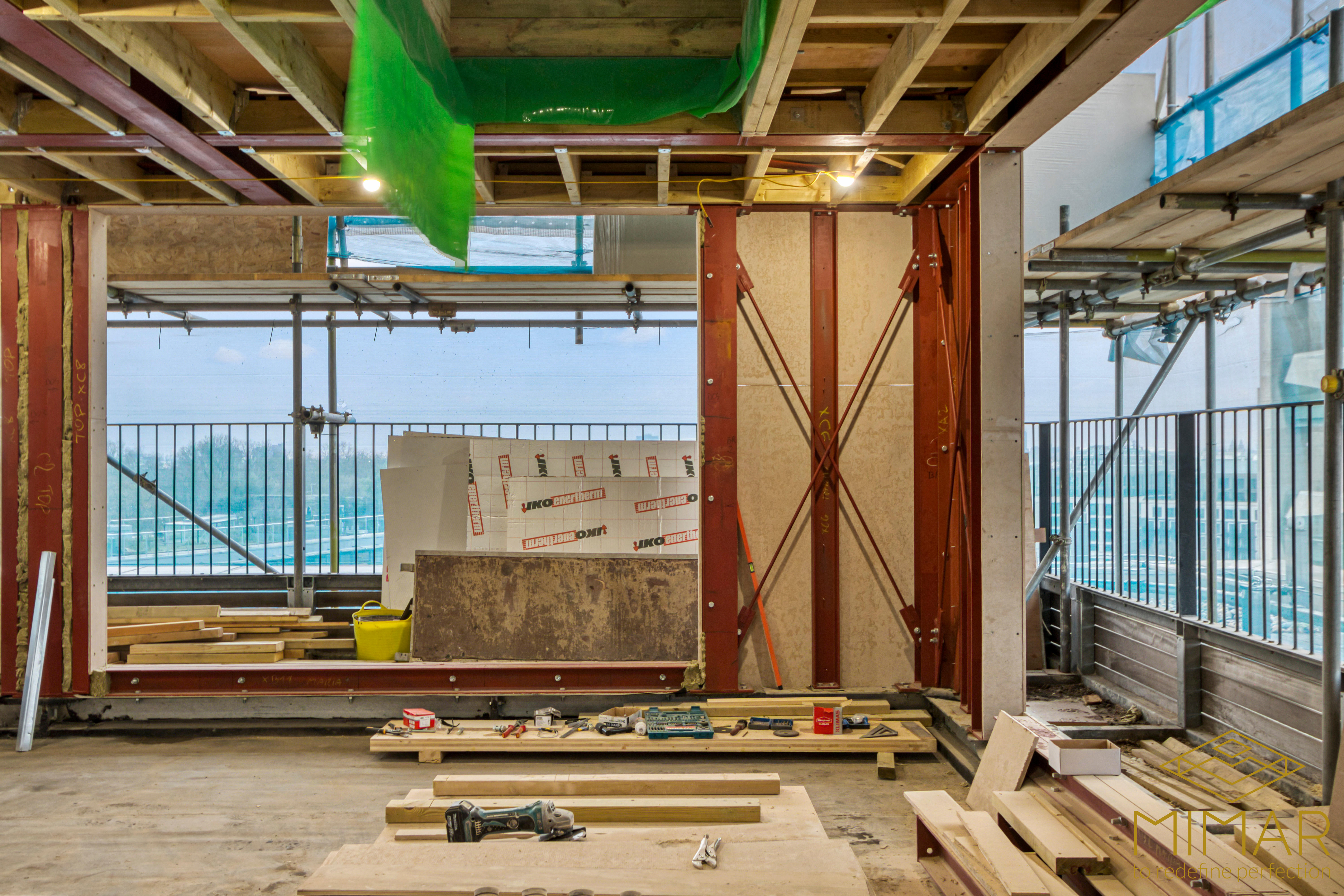Construction site showing steel beam framework and various construction materials and tools, indicating an extension project in progress.