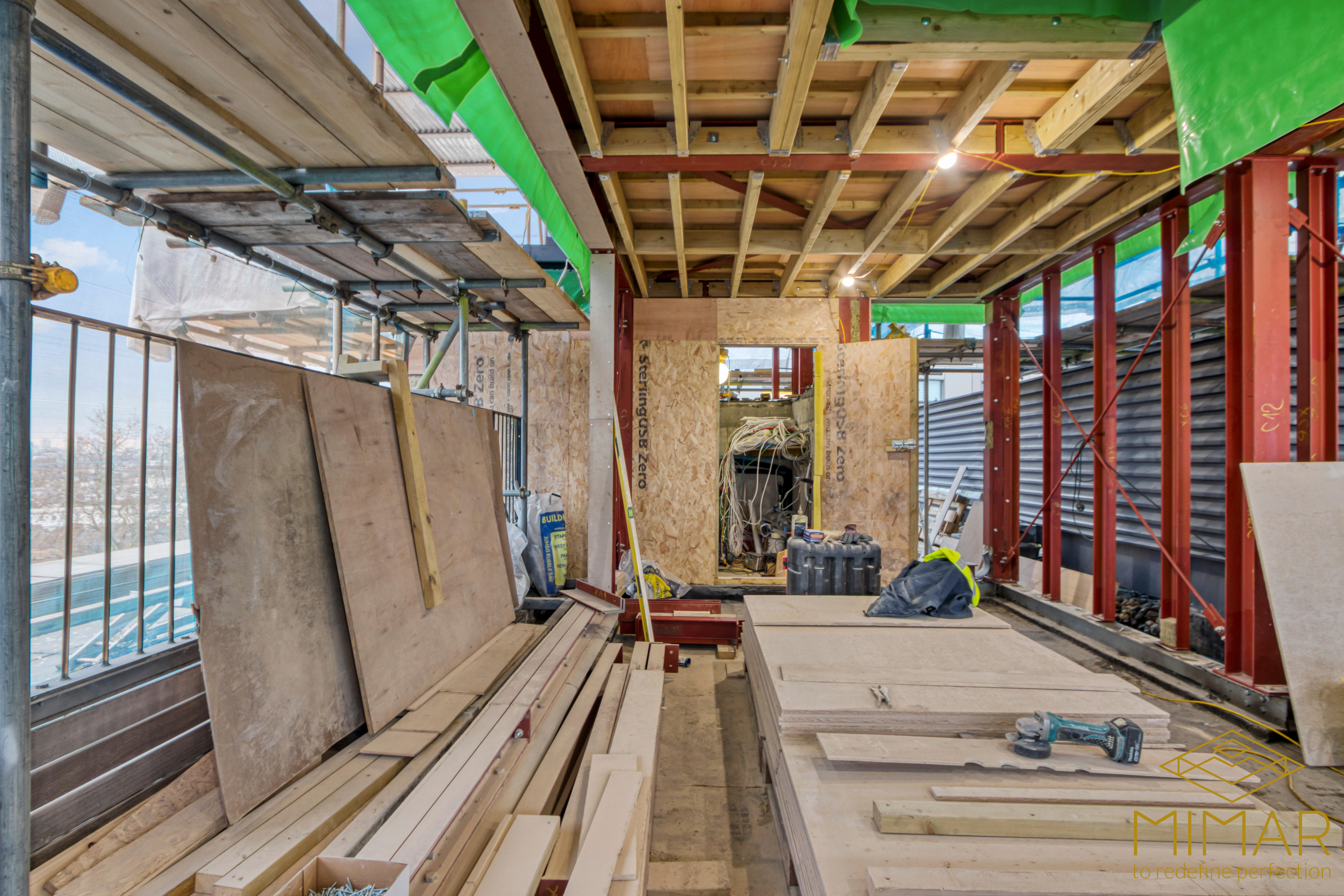 The interior of a house extension under construction, featuring scaffolding, wood panels, and construction materials.