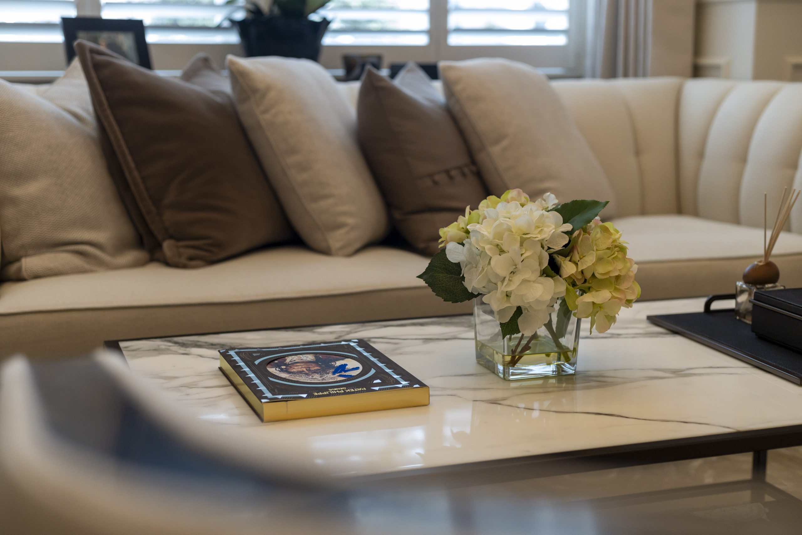 A stylish living room with a cream sofa, decorative cushions, a marble coffee table, and a vase of flowers, indicating a home renovation.