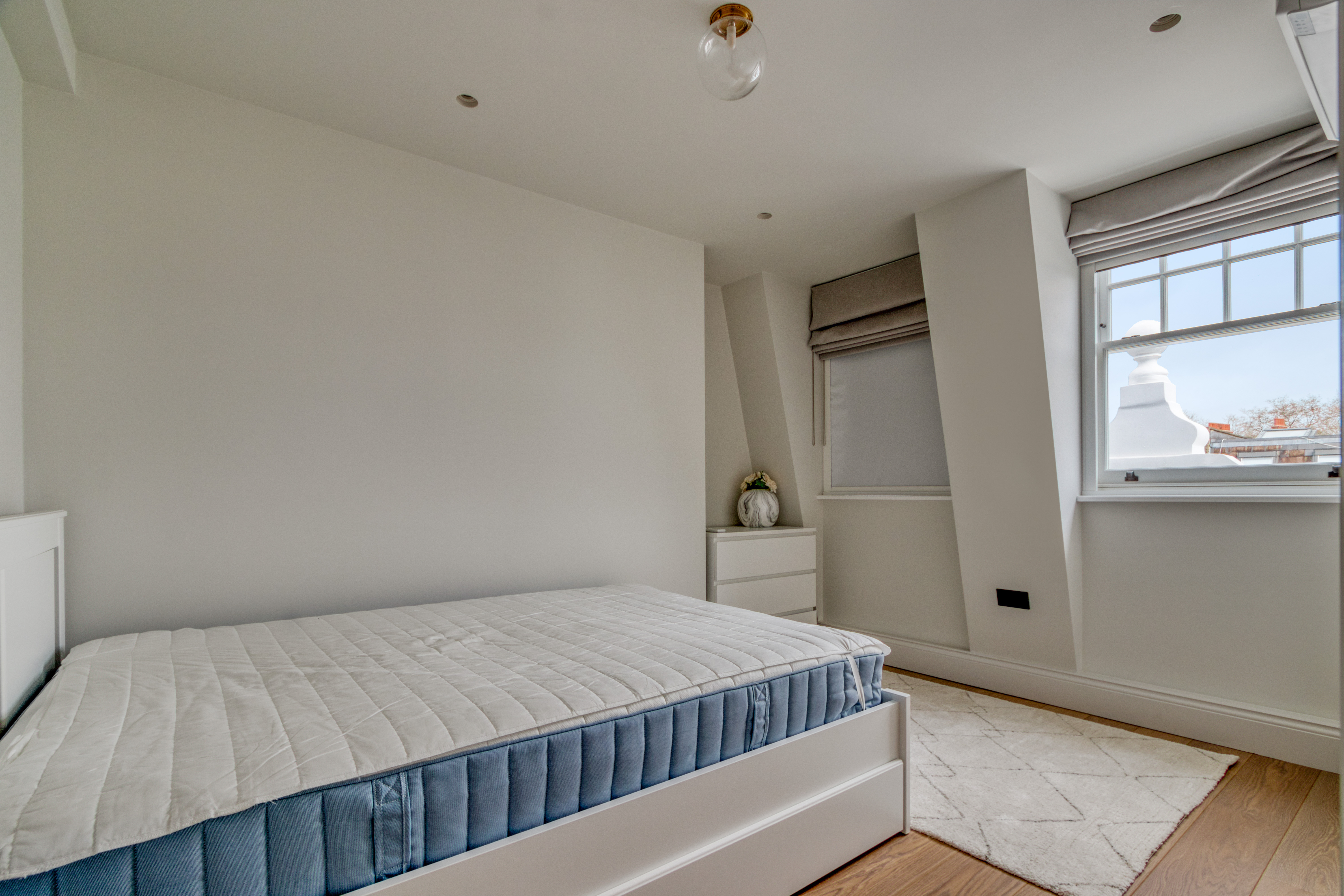 A newly refurbished loft bedroom with a bed, window, and dresser in a compact space.