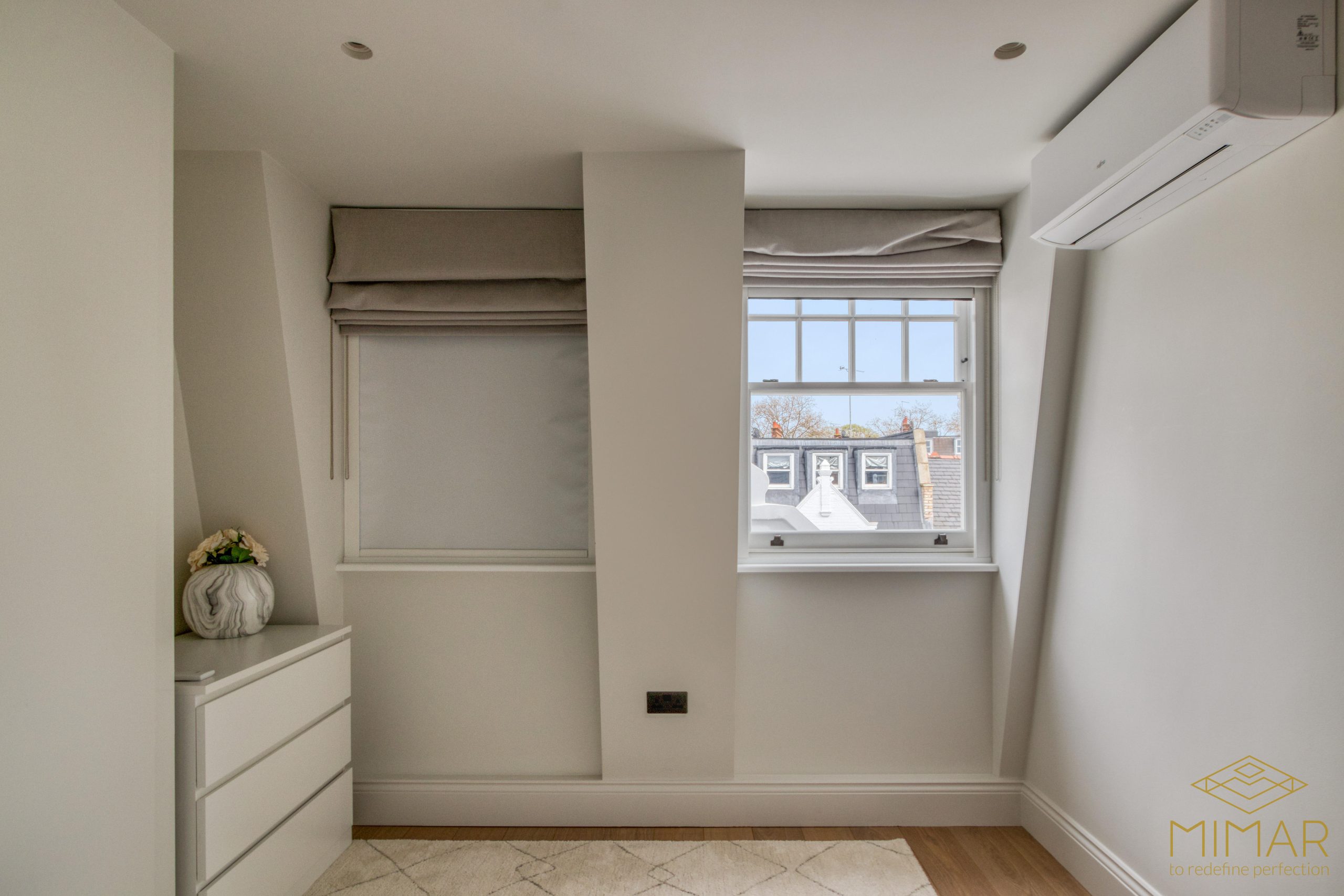 Interior view of a small loft room with dormer windows, minimalist decor, and an air conditioning unit.