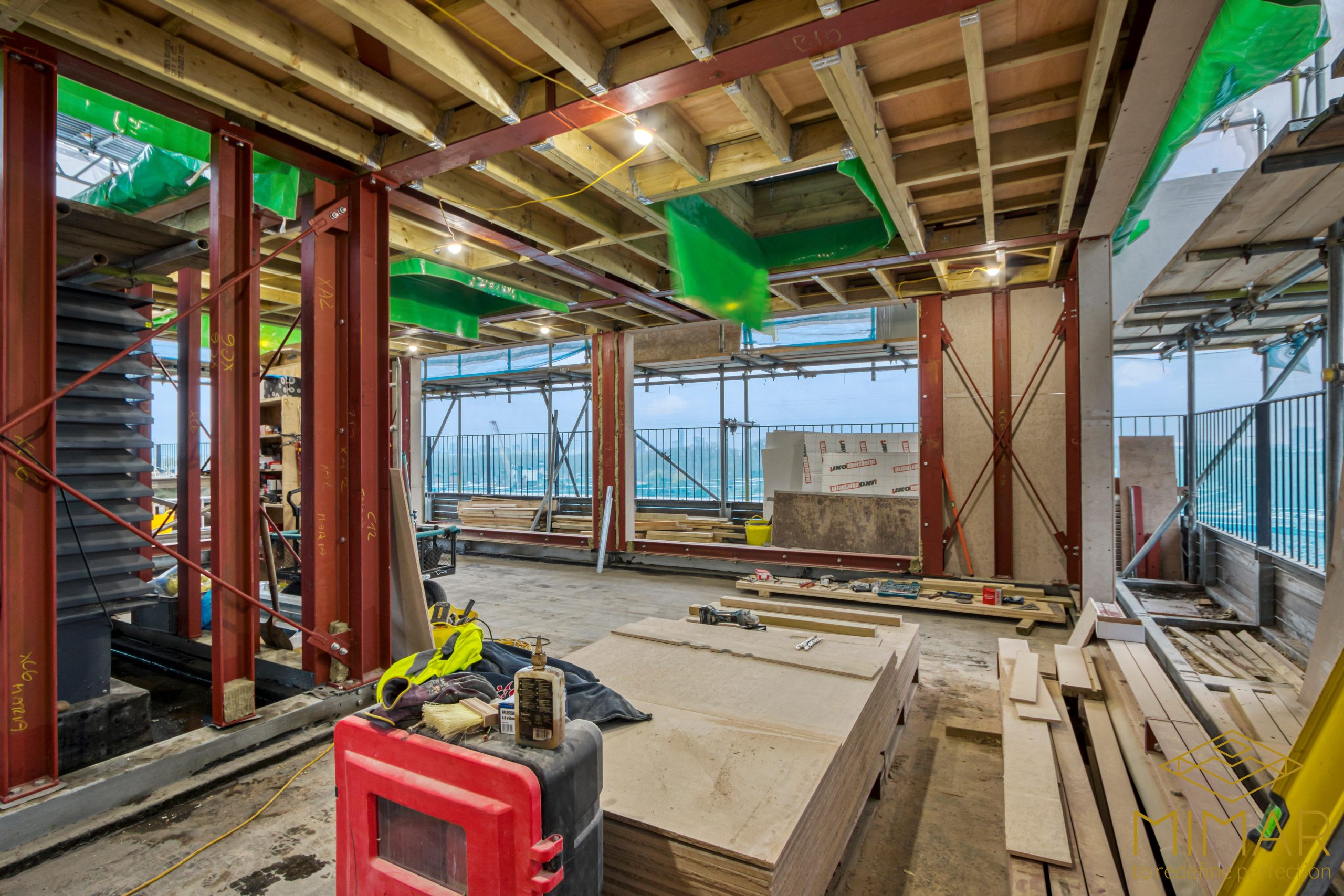 Interior view of a loft space under construction, featuring wooden framing, steel beams, and construction materials on-site.