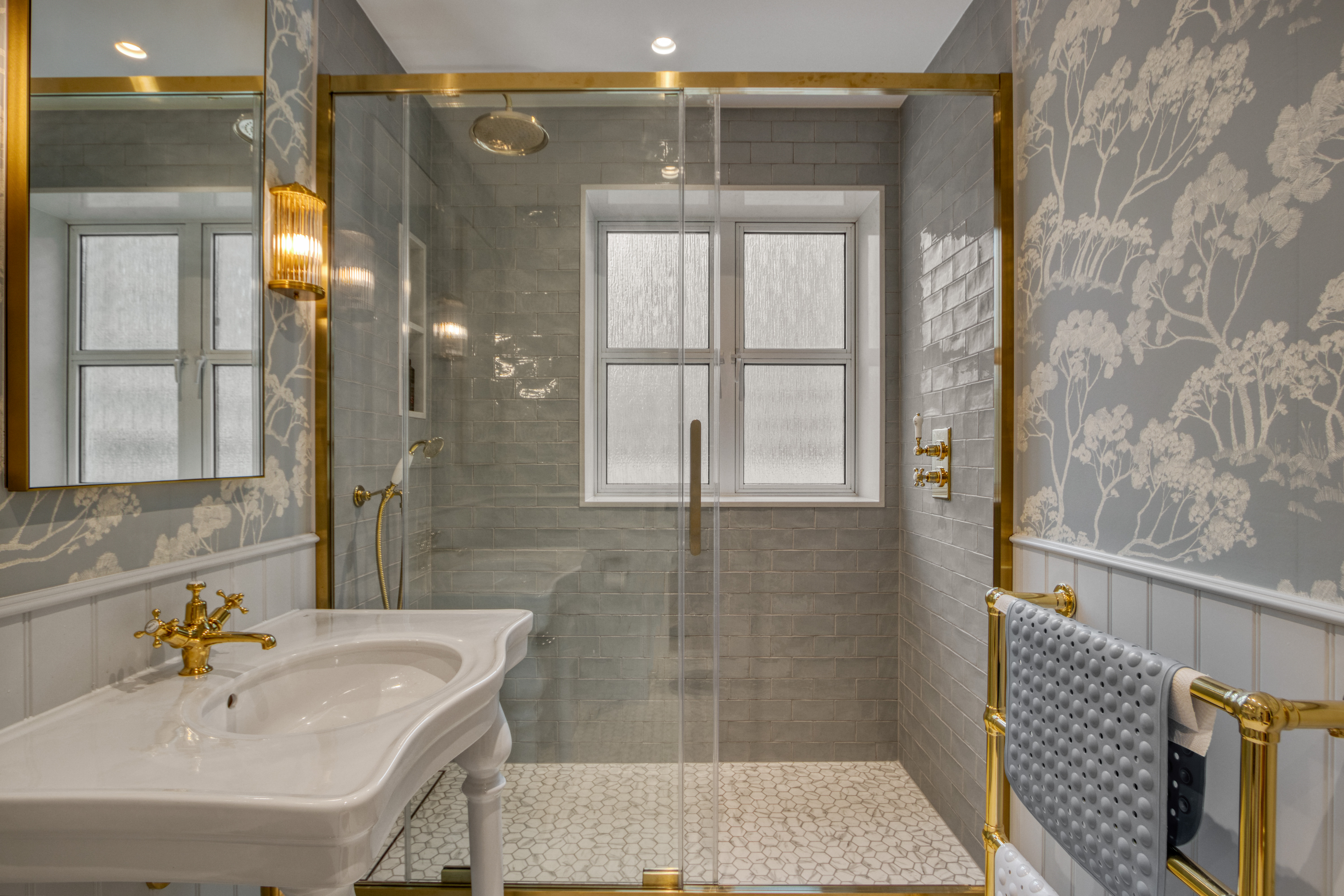 A modern bathroom with a glass-enclosed shower, gold fixtures, and stylish wallpaper.