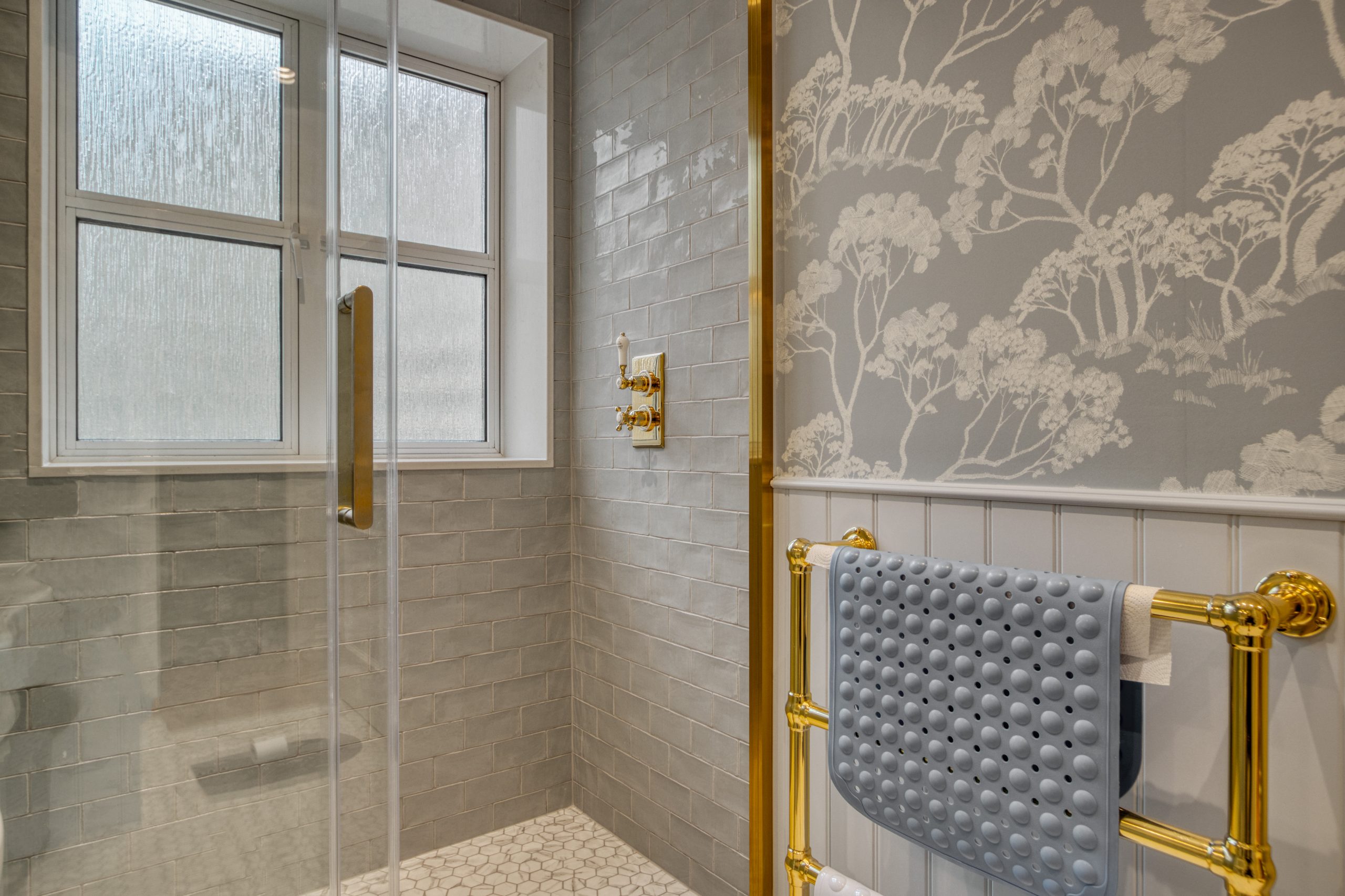 A bathroom showcasing a glass shower enclosure with tiled walls, a decorative towel warmer, and patterned wallpaper.
