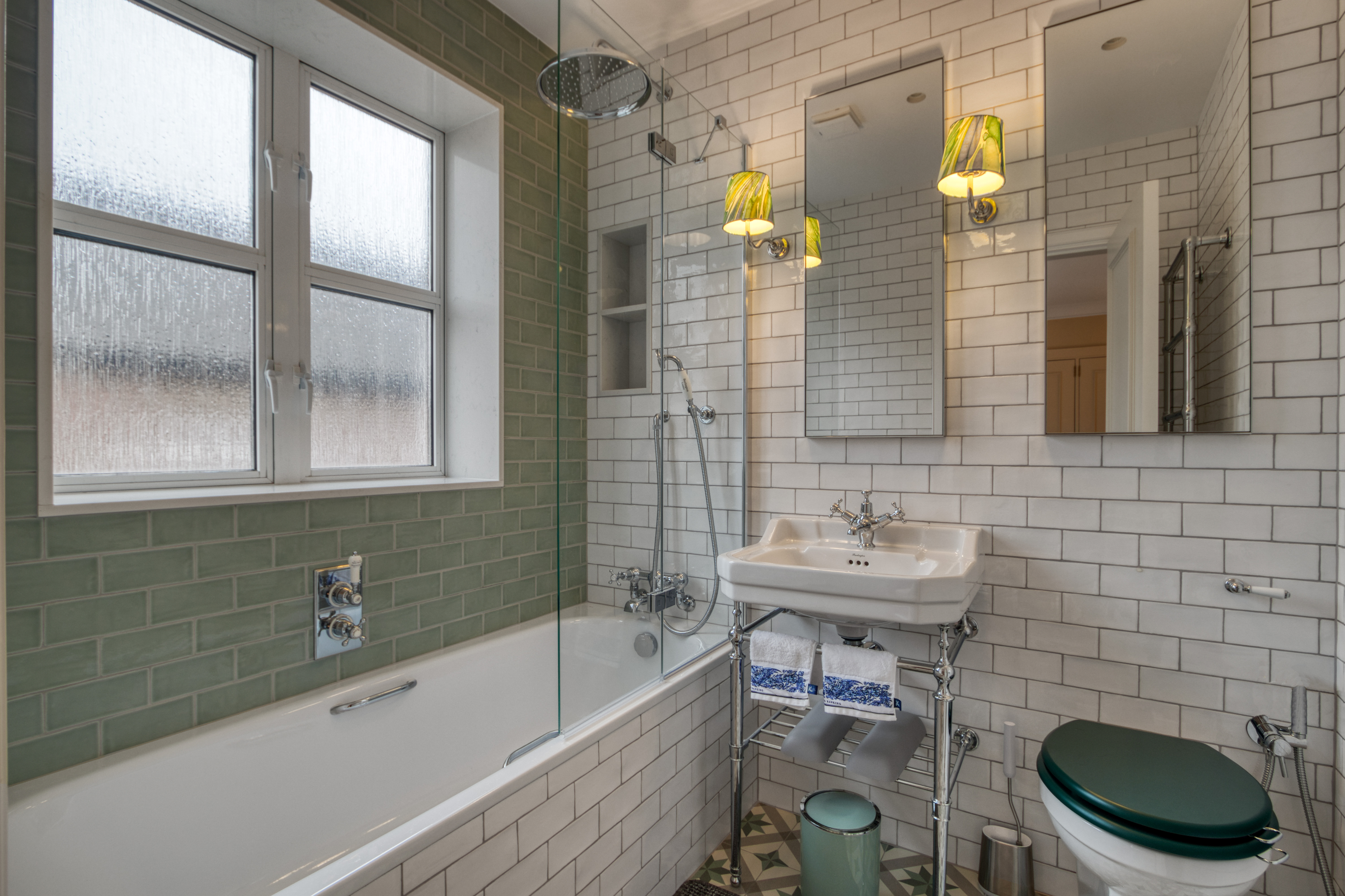 A renovated bathroom featuring a white bathtub, green and white tiles, a wall-mounted shower, a mirrored vanity, and a modern sink with stylish fixtures.