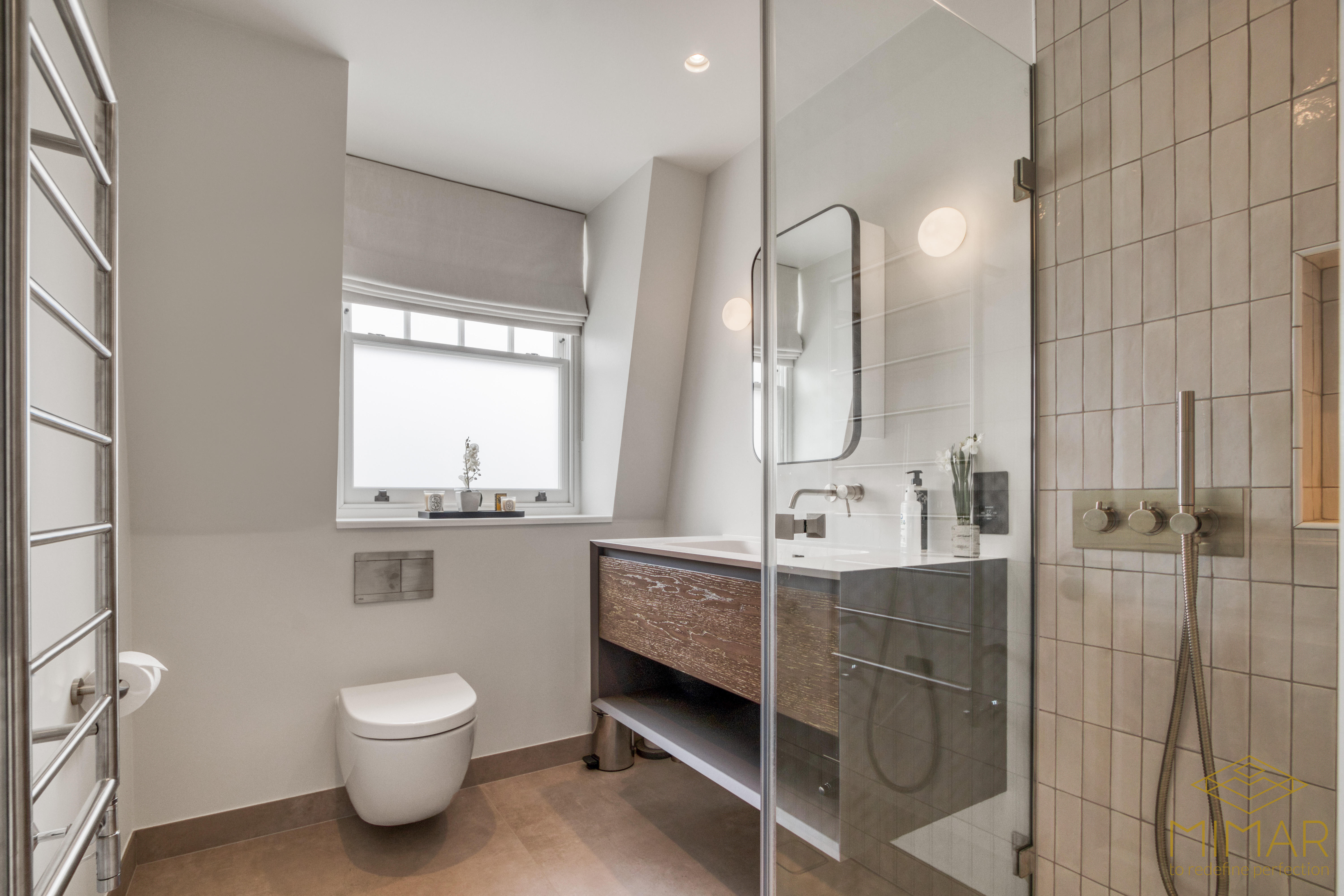 A modern bathroom with a glass shower, wall-mounted toilet, and contemporary vanity under a window with a blind.