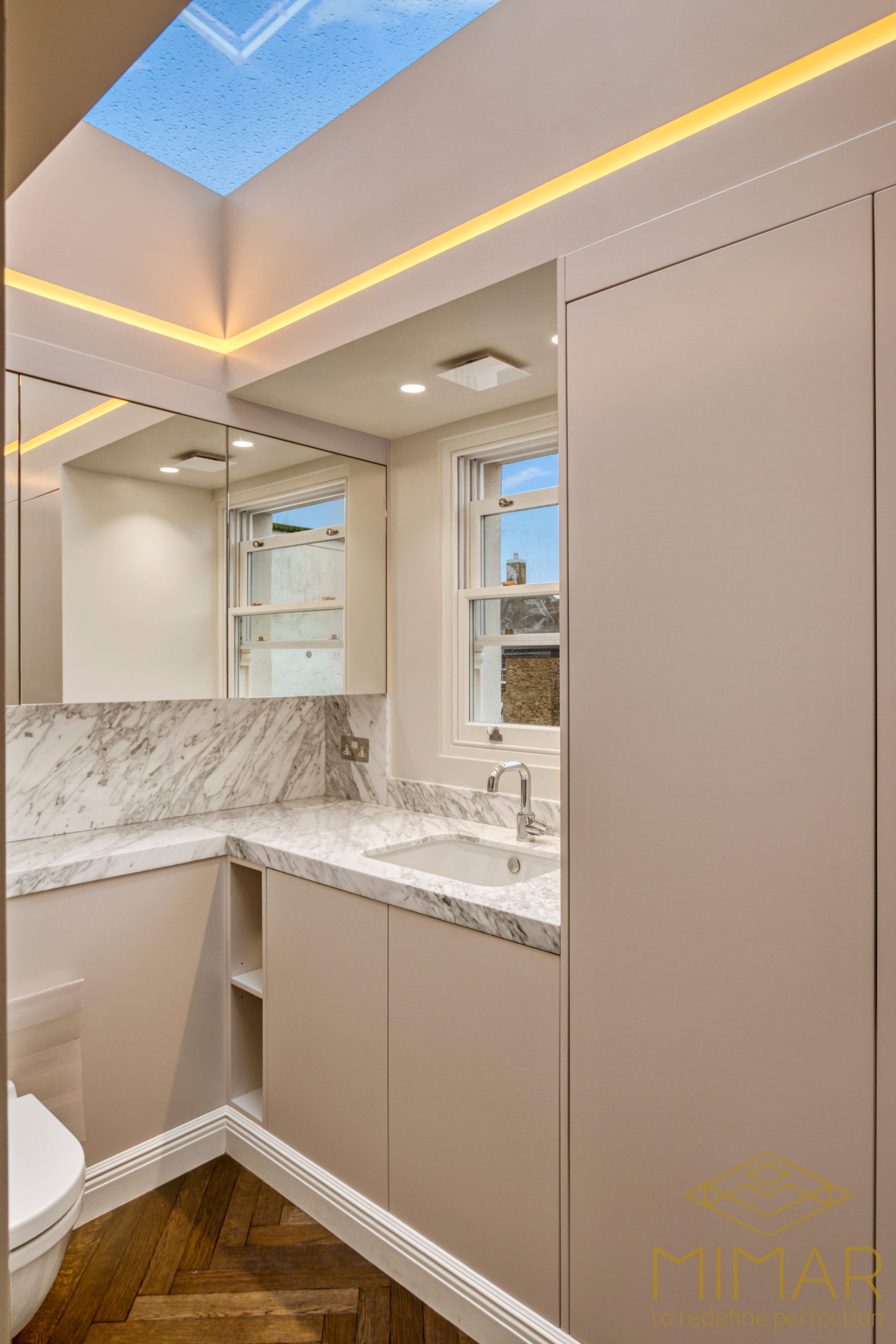 A modern bathroom featuring marble countertops, a skylight, and a sleek sink area with integrated cabinetry.
