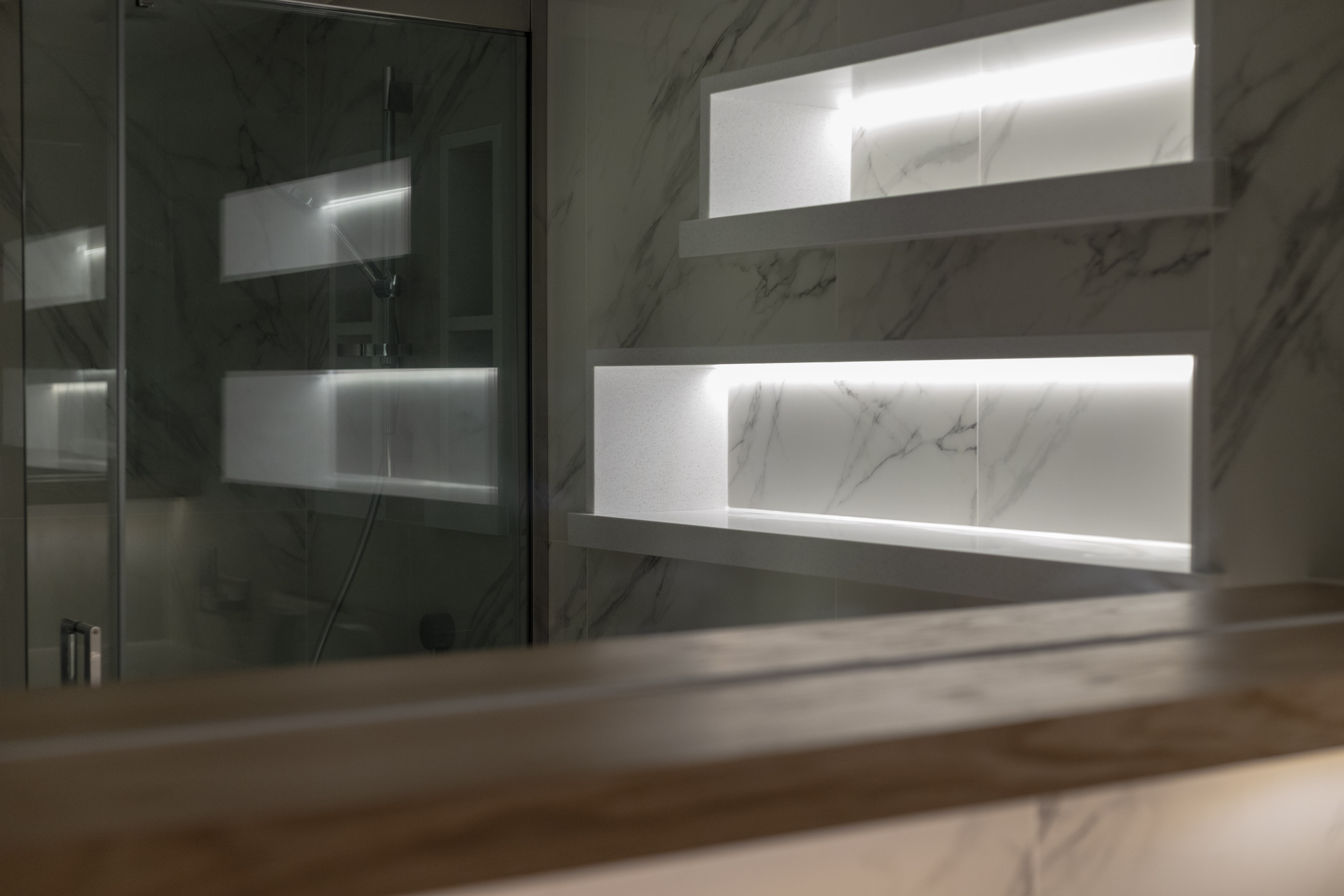 Modern bathroom with illuminated recessed shelves and marble walls.