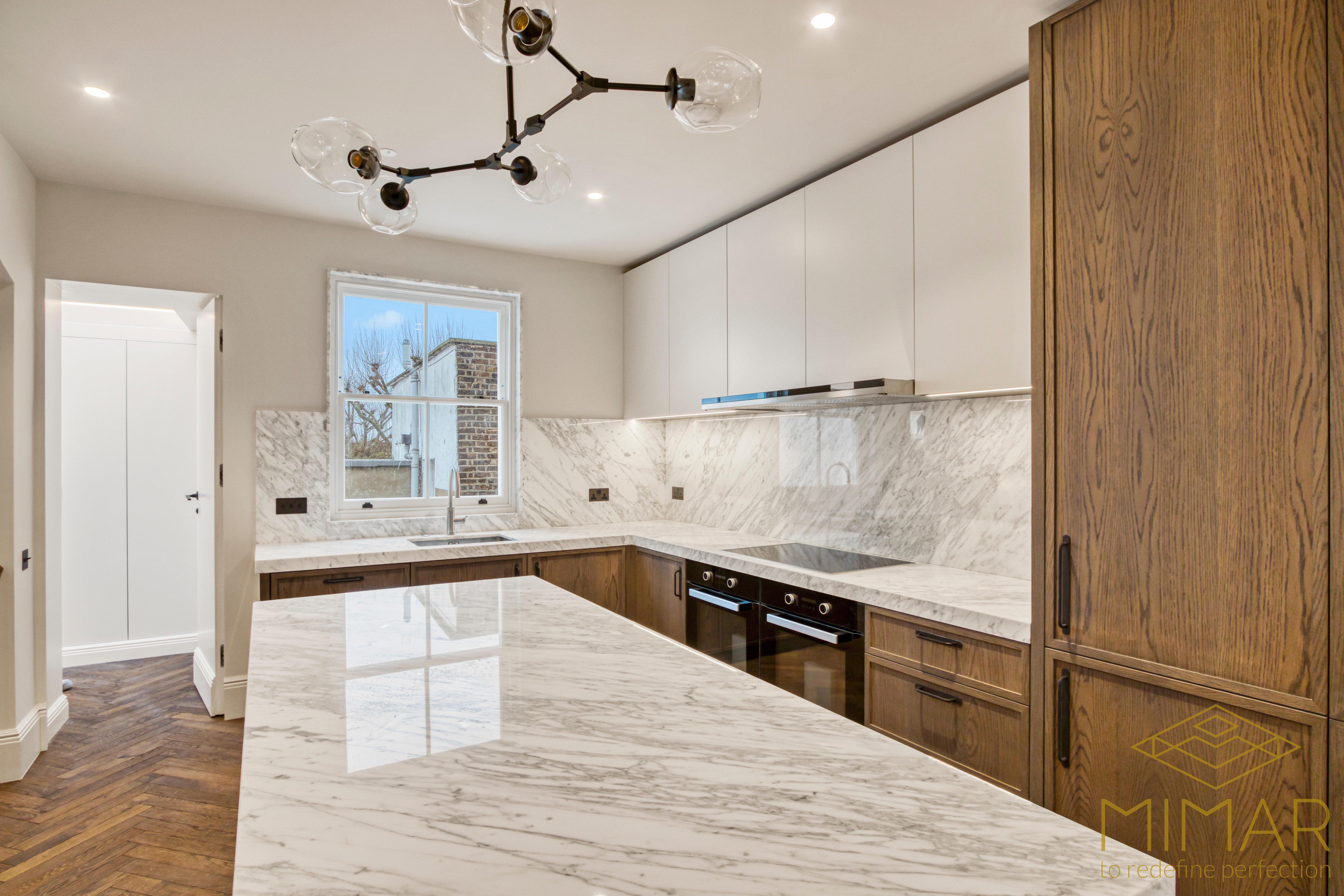 A modern kitchen featuring marble countertops and backsplash, sleek wooden cabinets, and contemporary lighting fixtures.