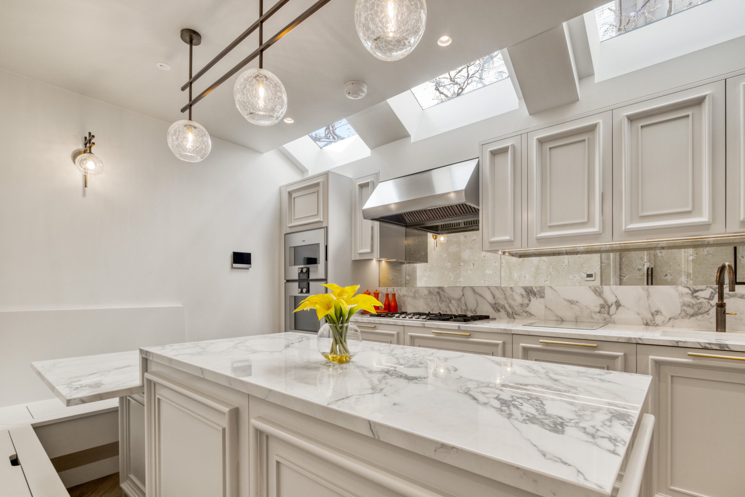 A modern kitchen with white marble countertops and island, integrated appliances, and pendant lighting under skylights.