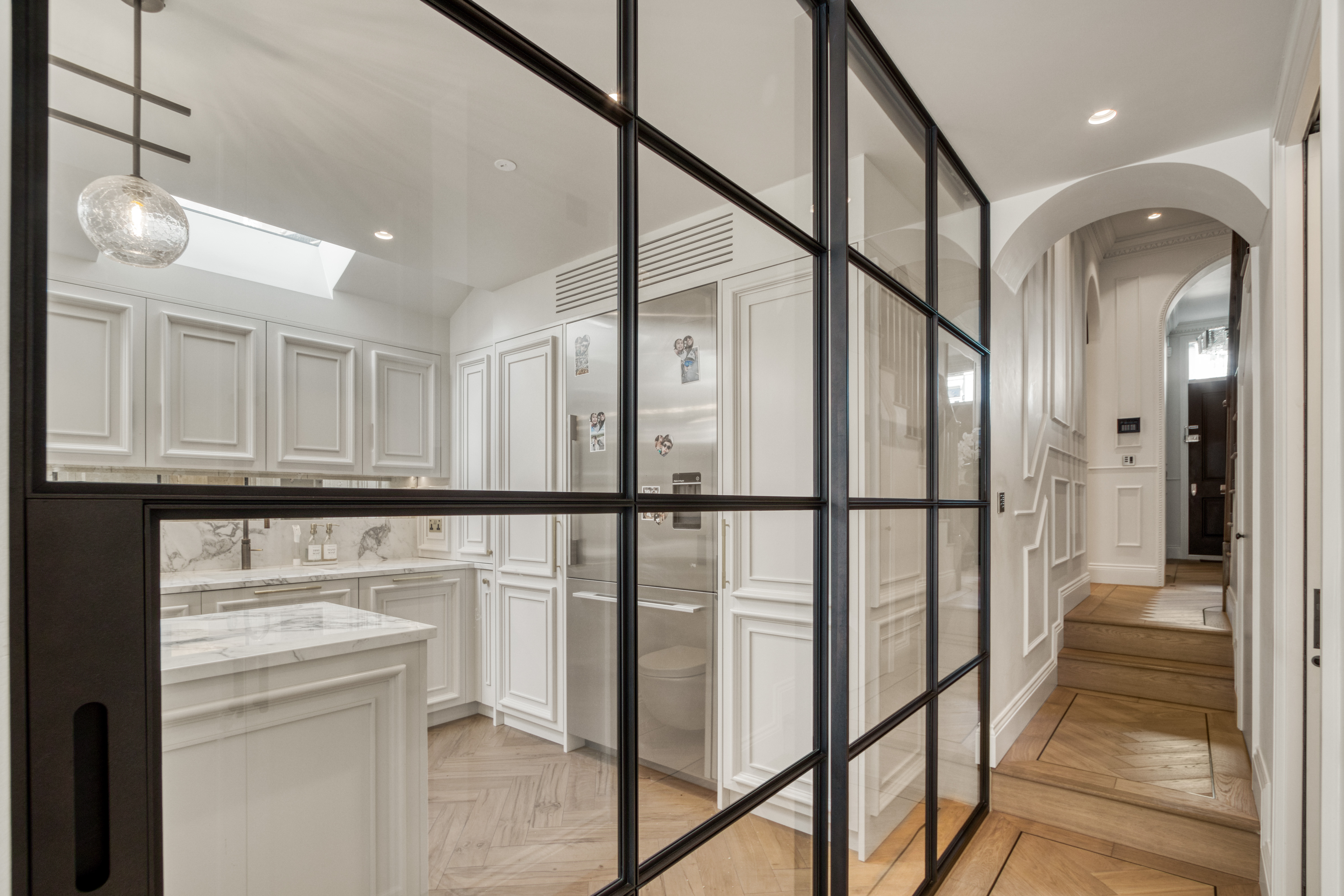 Modern kitchen with white cabinetry, marble countertops, and glass partition in a renovated home.