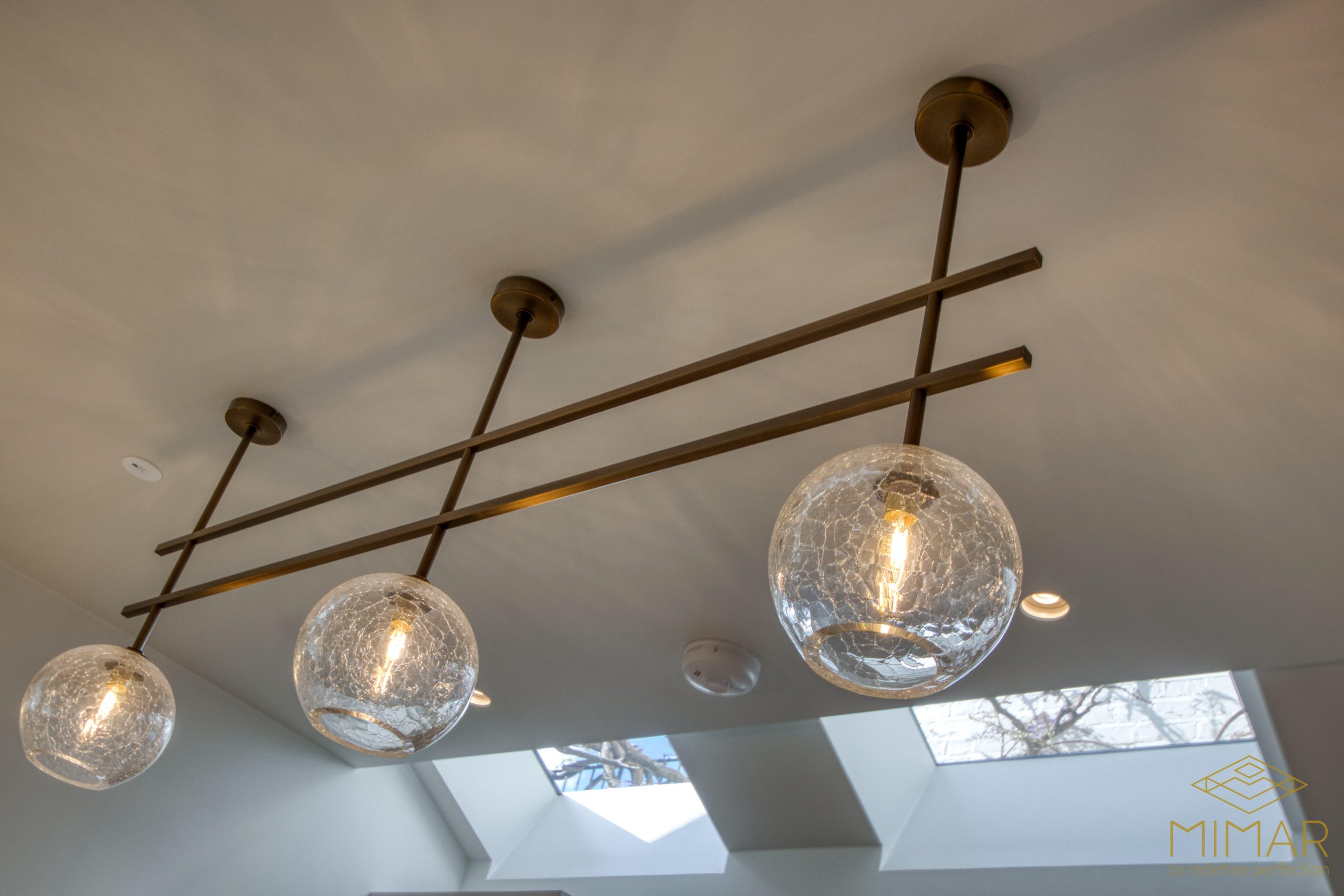 Contemporary ceiling light fixture installation featuring three glass globe pendants and skylights in the background.