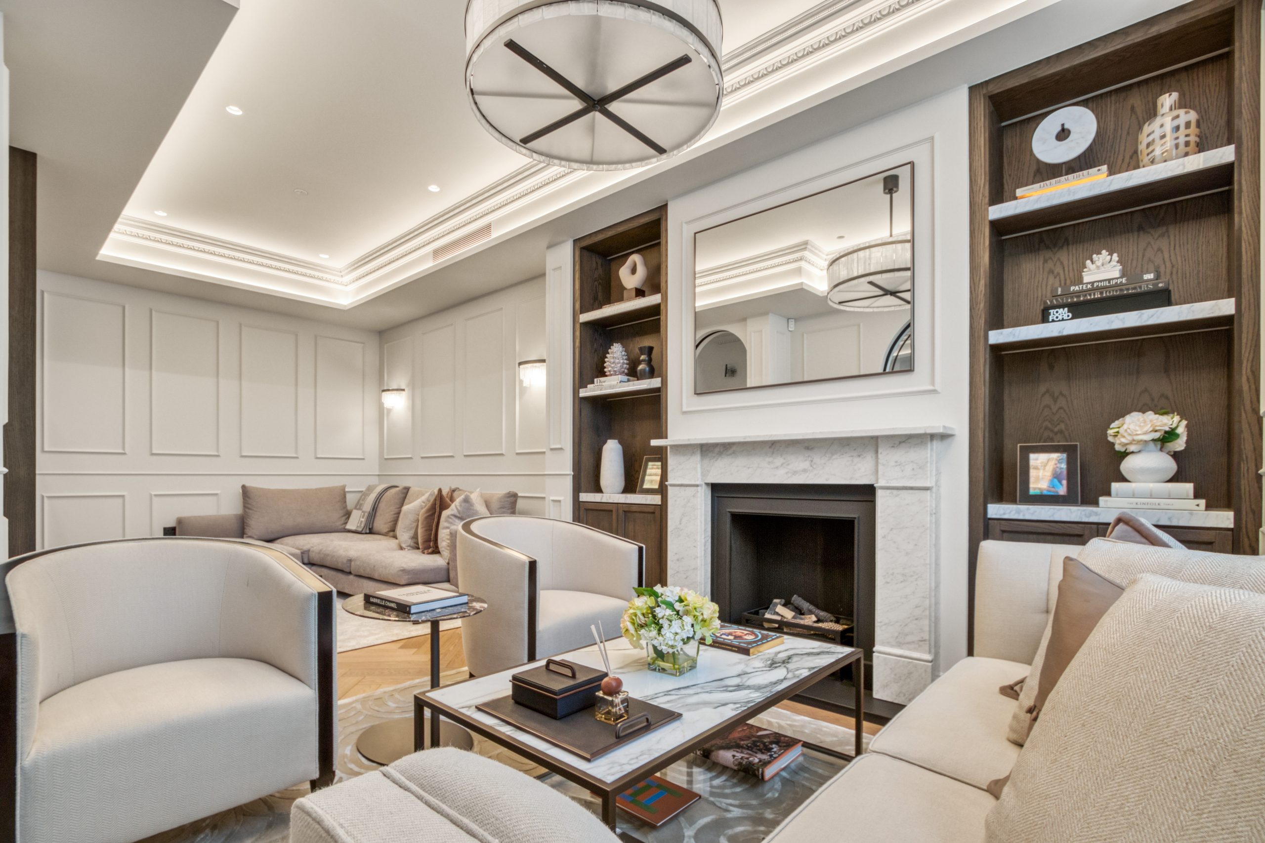 A modern living room with elegant white paneling, comfortable seating, built-in shelving, and a sophisticated lighting fixture.