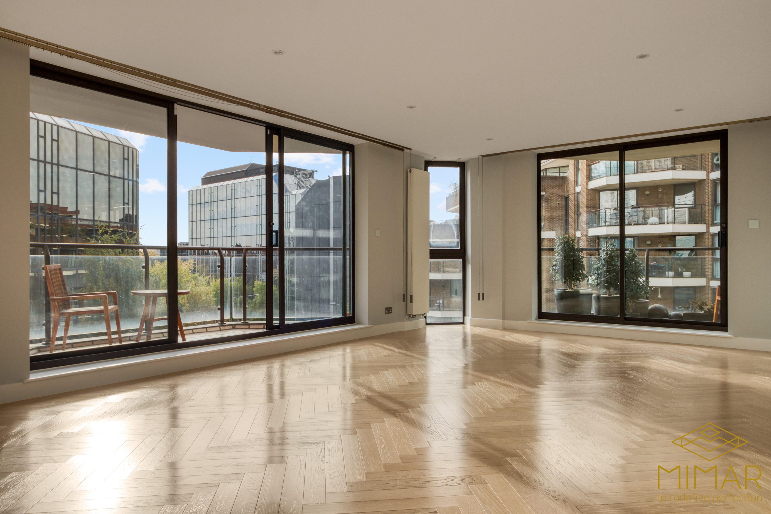 Spacious refurbished living area with large floor-to-ceiling windows and herringbone wood flooring.
