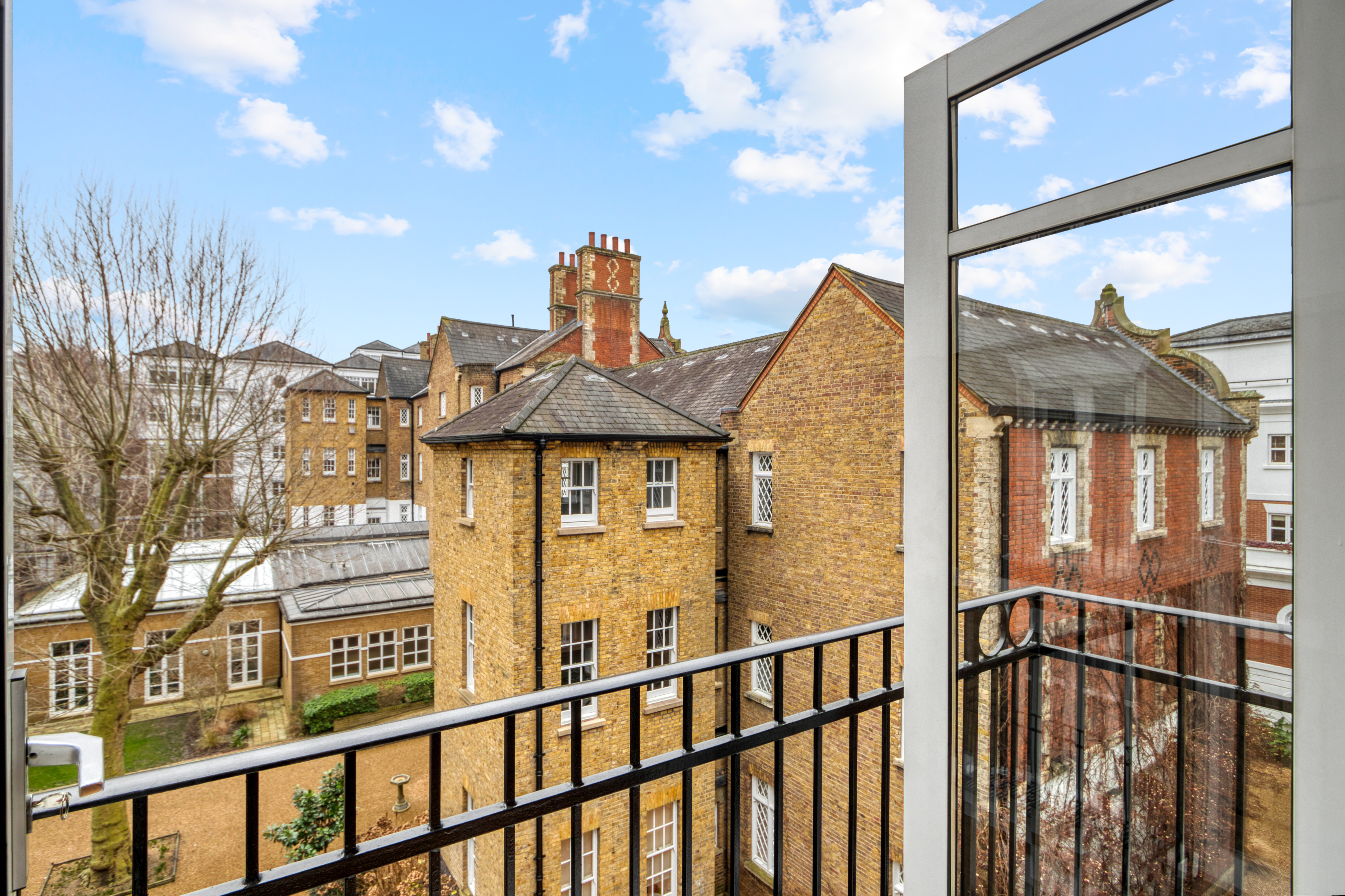 View from a residential balcony overlooking historic brick buildings with a metal railing in the foreground.