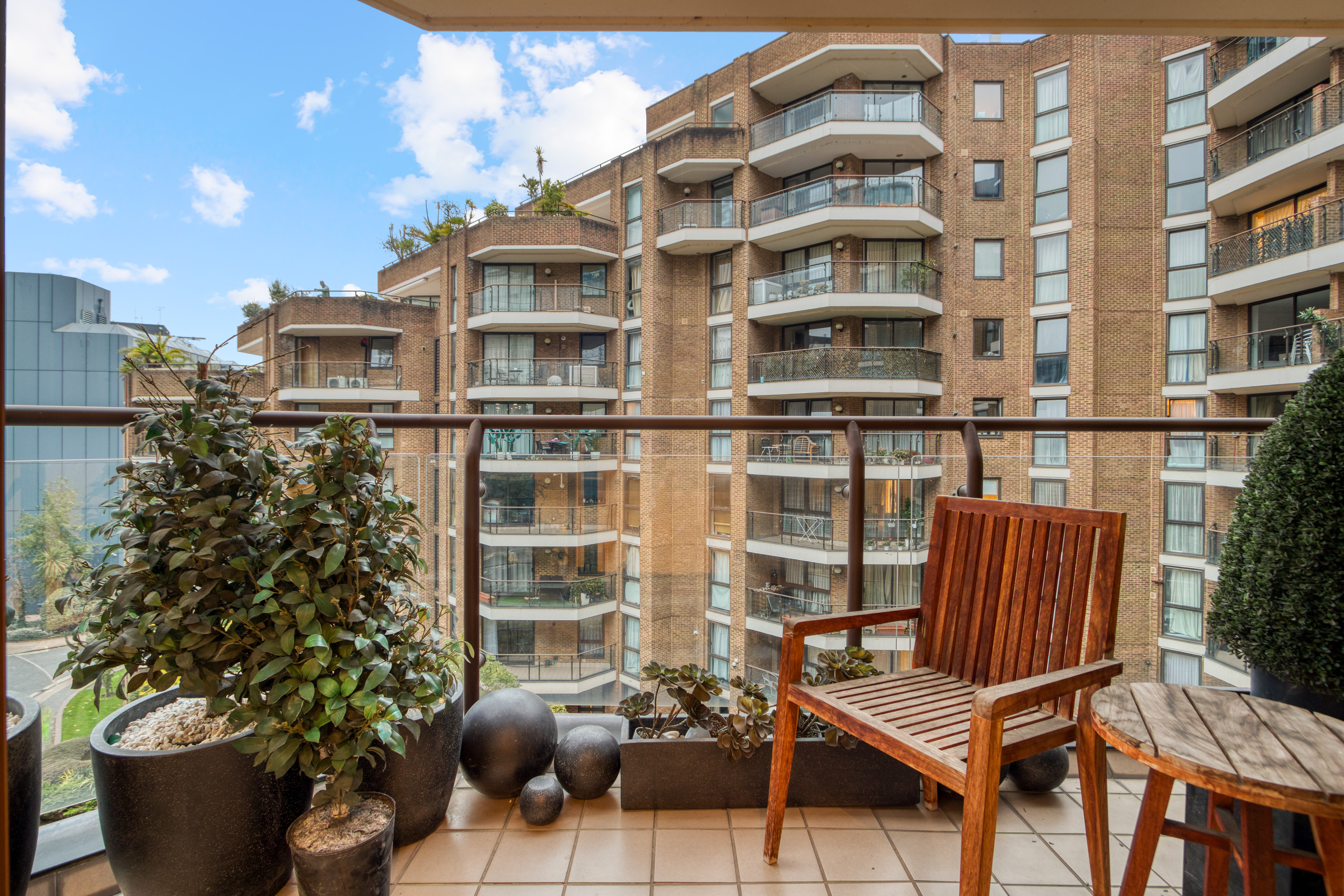 A balcony with wooden furniture and plants overlooking modern residential buildings.