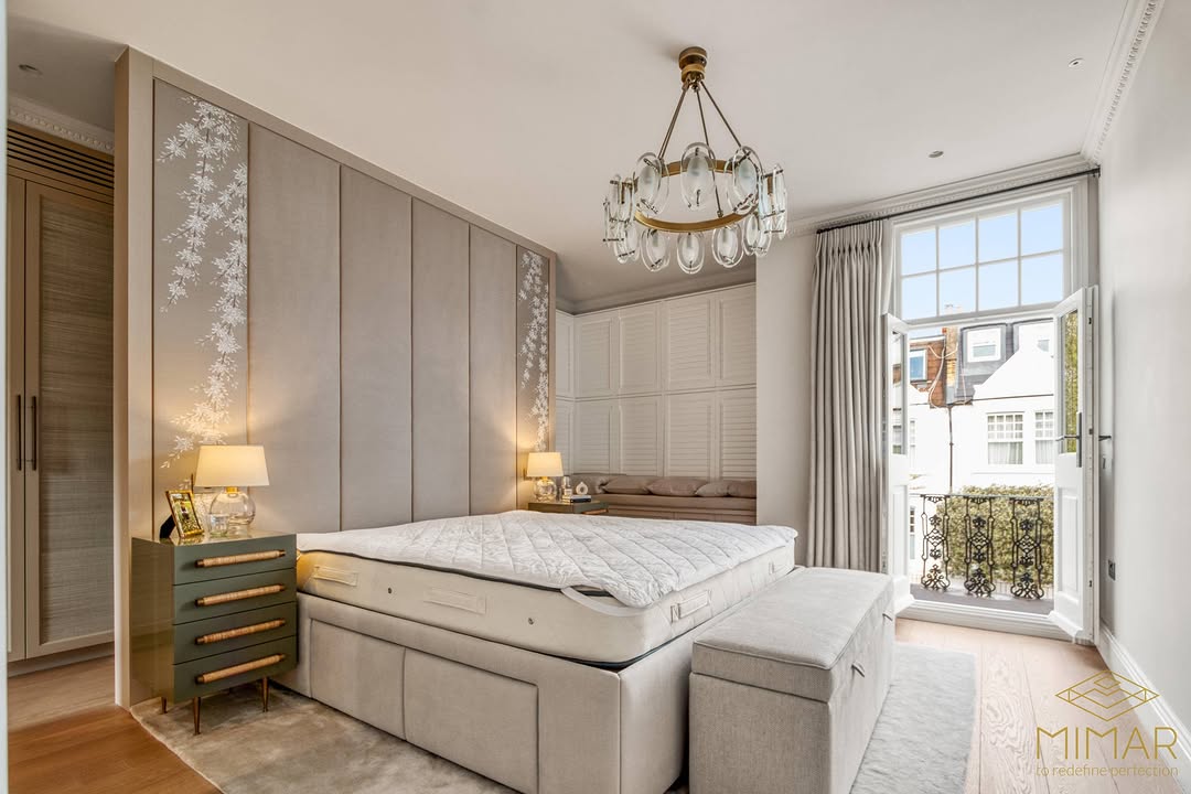 A modern, elegantly remodeled bedroom with a large bed, stylish chandelier, and opened French doors leading to a balcony.