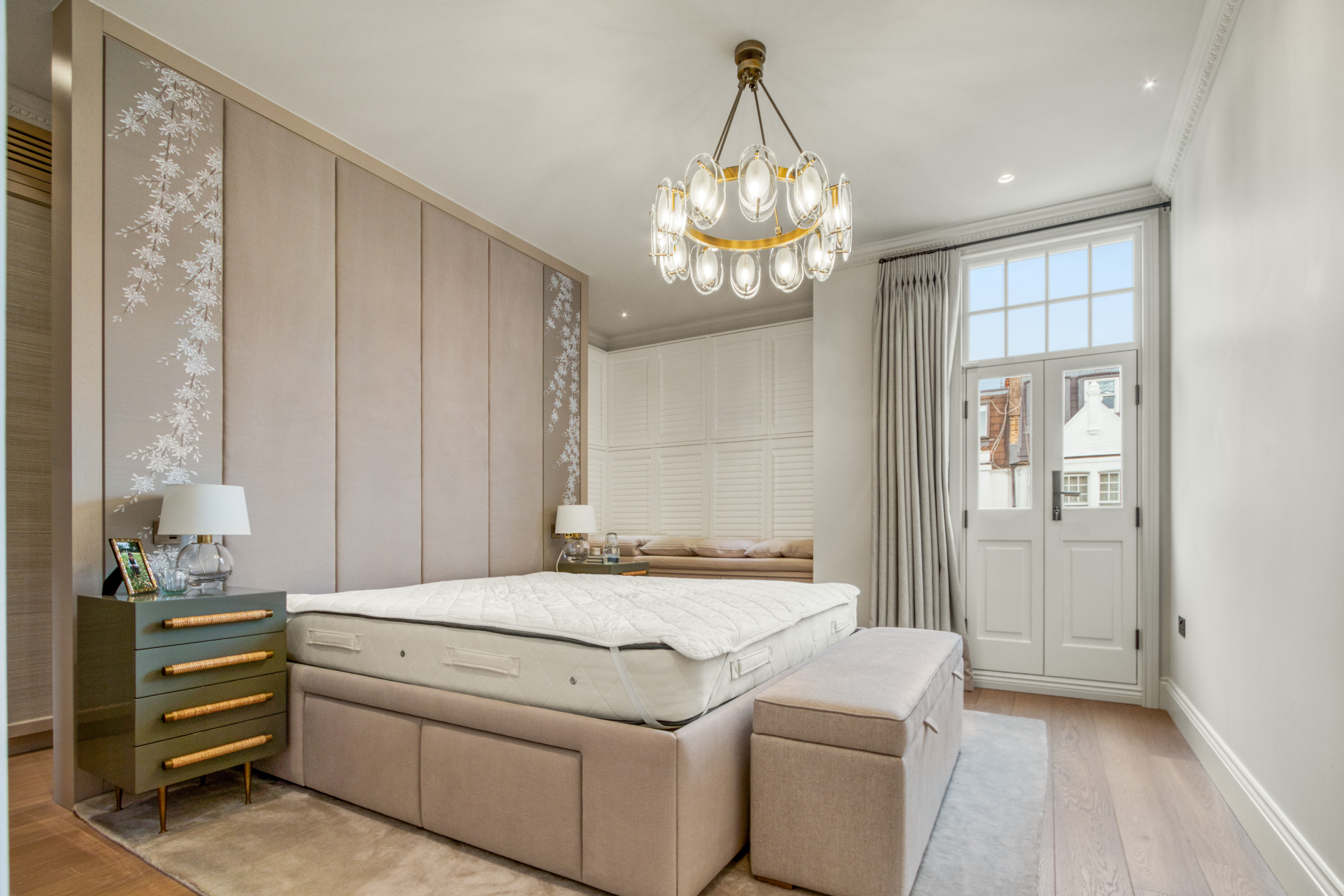 Modern, elegantly designed bedroom with upholstered walls, a chandelier, and large window doors.