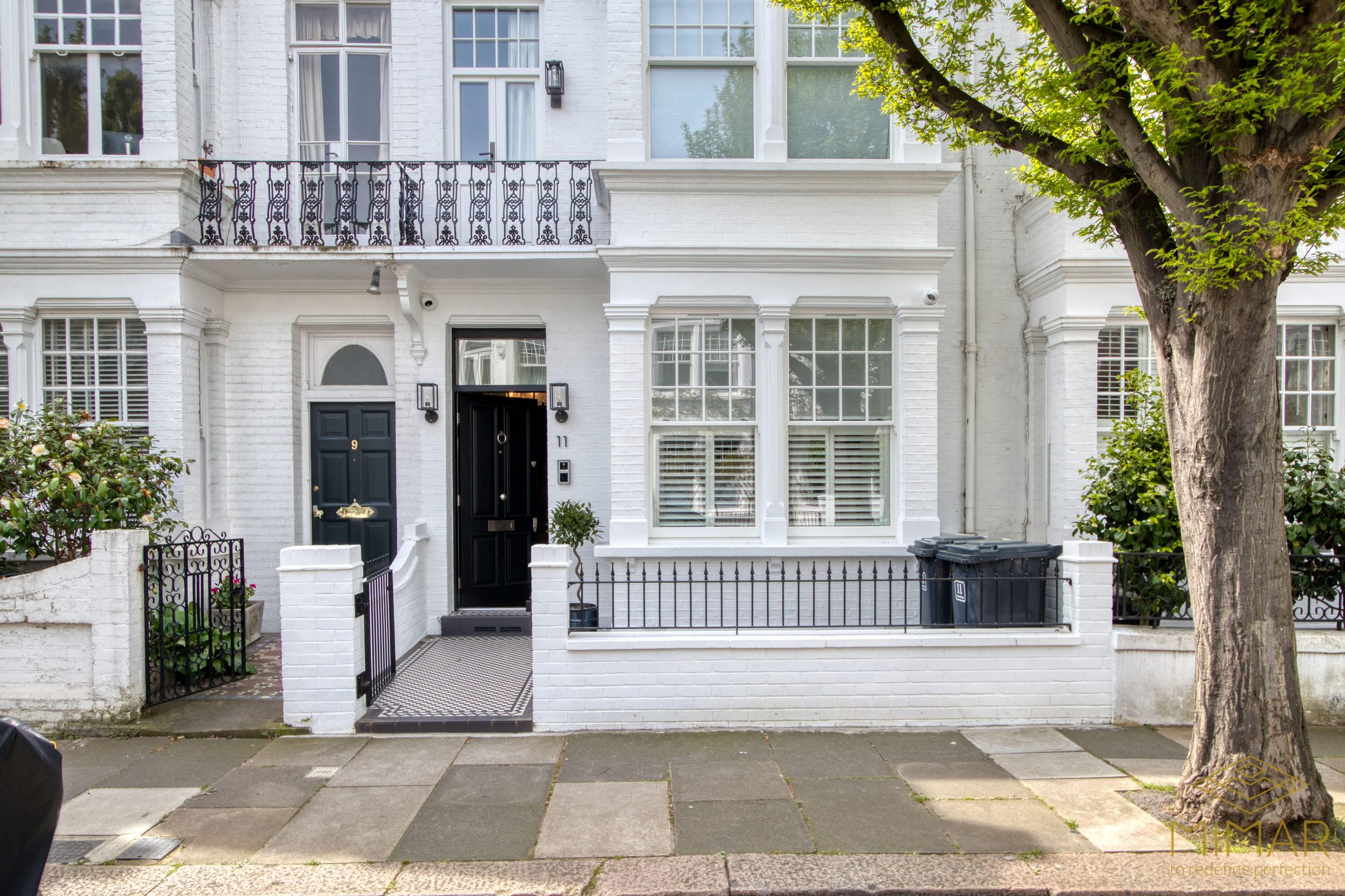 Front view of a refurbished white brick townhouse with black doors and ornate ironwork balcony.