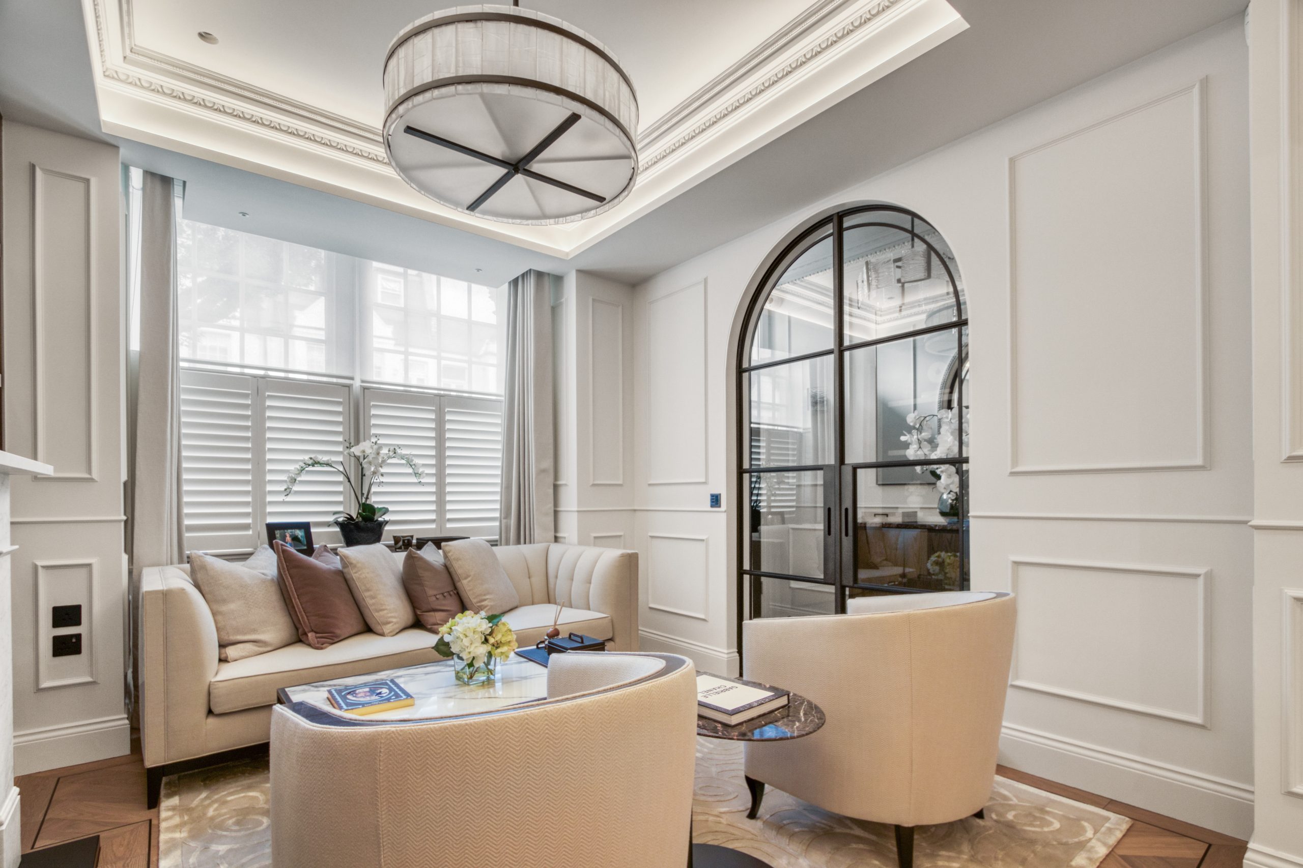 Elegant living room with modern furnishings, featuring a large sofa, armchairs, decorative molding, and an arched glass door.