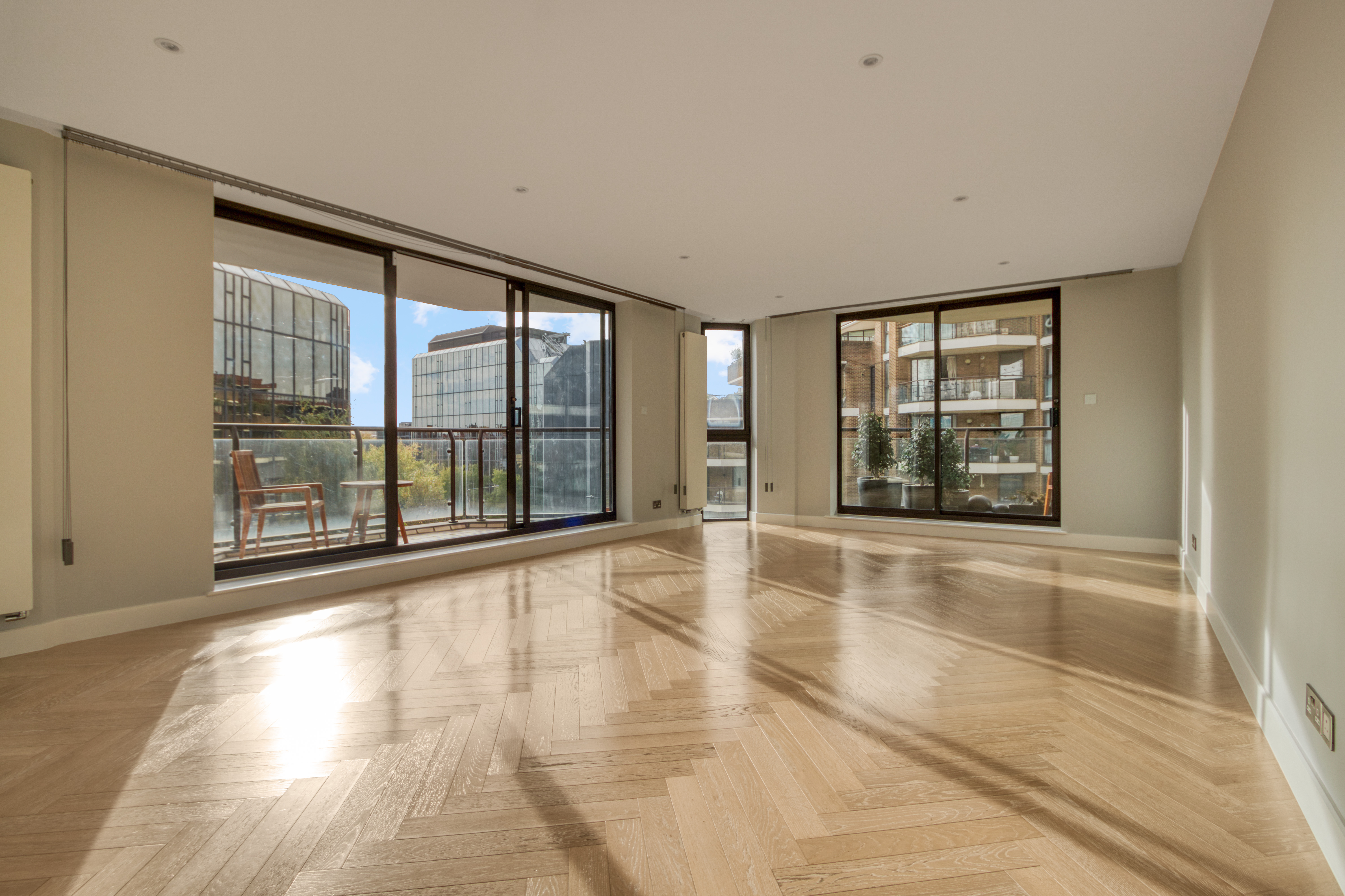 Spacious living room with large windows and wooden herringbone flooring in a refurbished residential apartment.