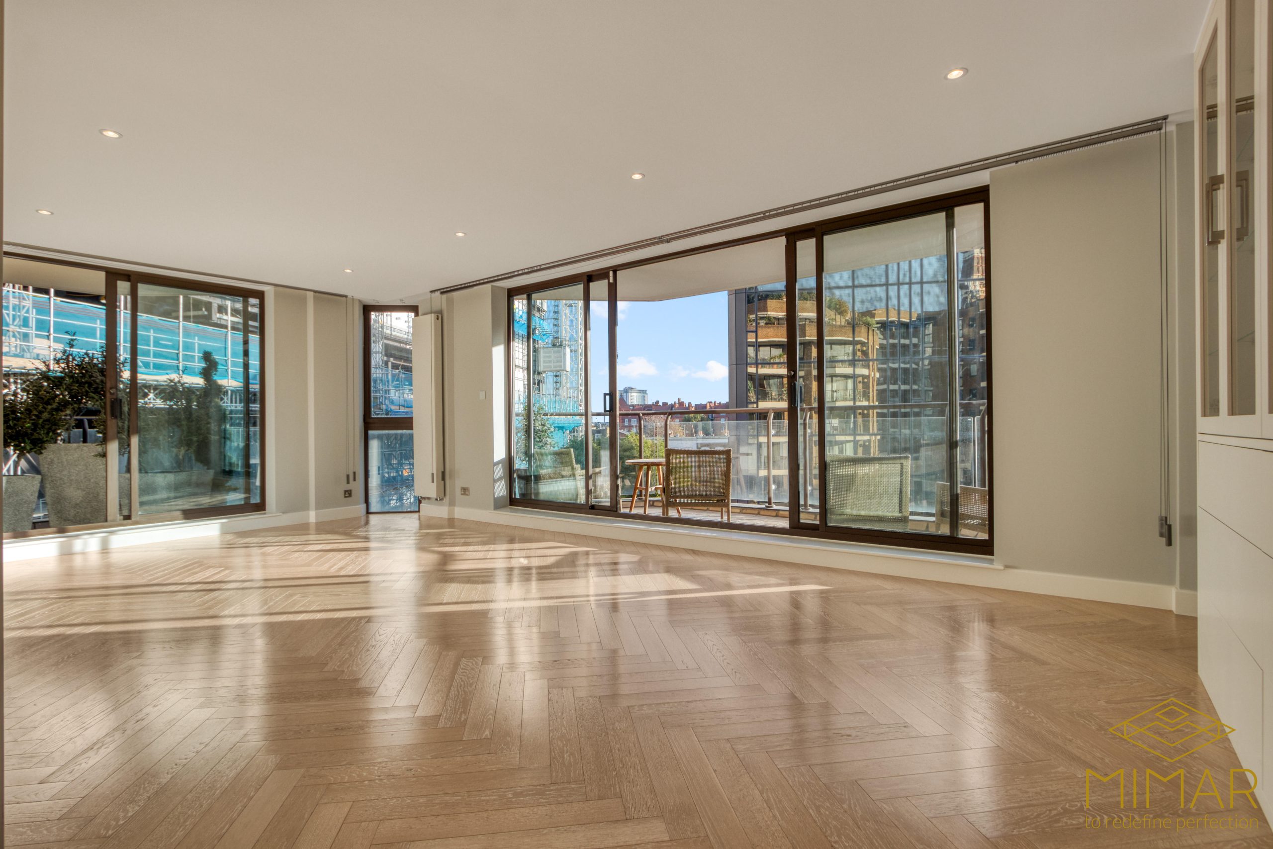 Spacious and bright living area with large sliding glass doors leading to a balcony, showcasing wooden herringbone flooring and modern fixtures.