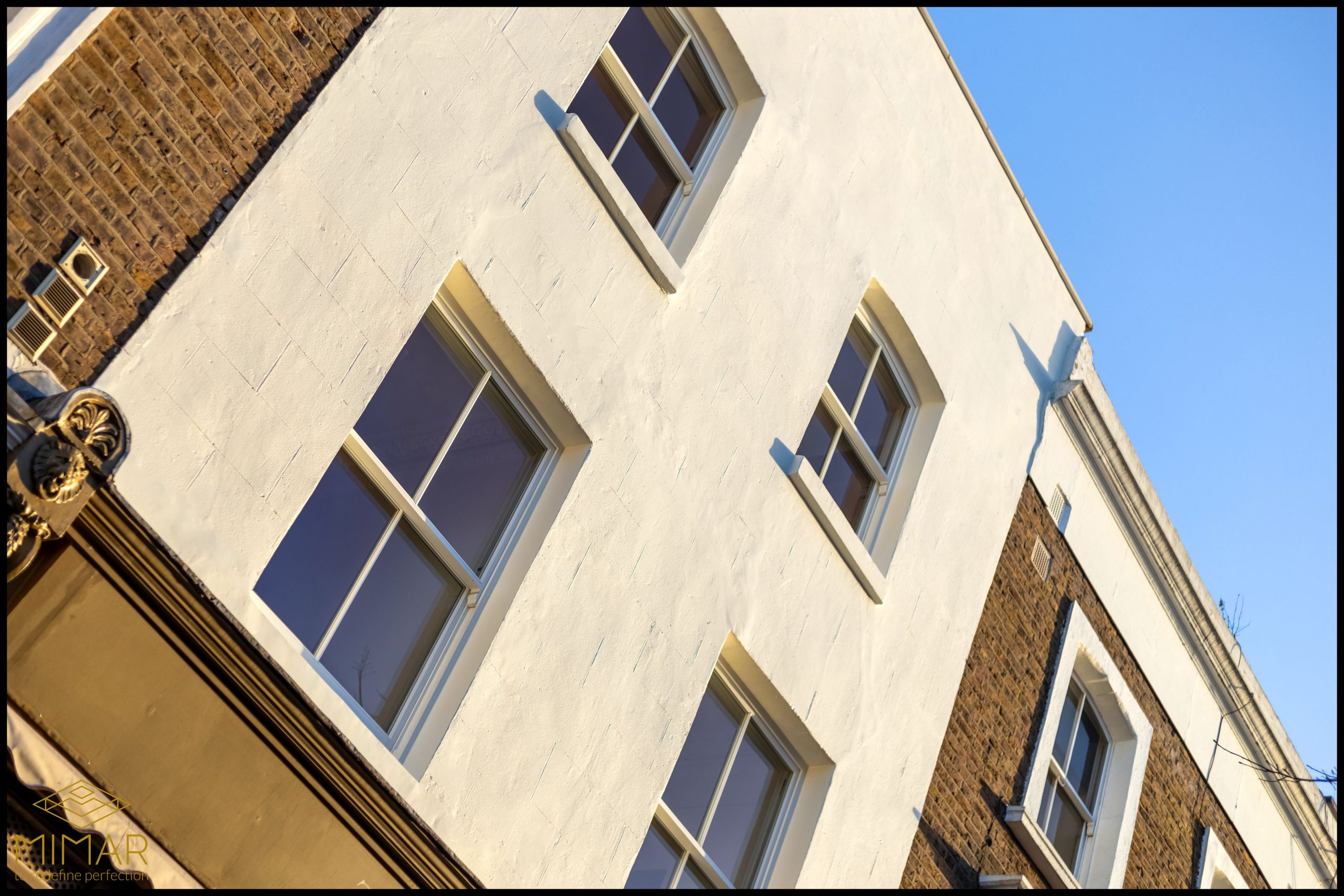 The image shows the refurbished exterior of a residential building with white and brick facades and multiple windows.
