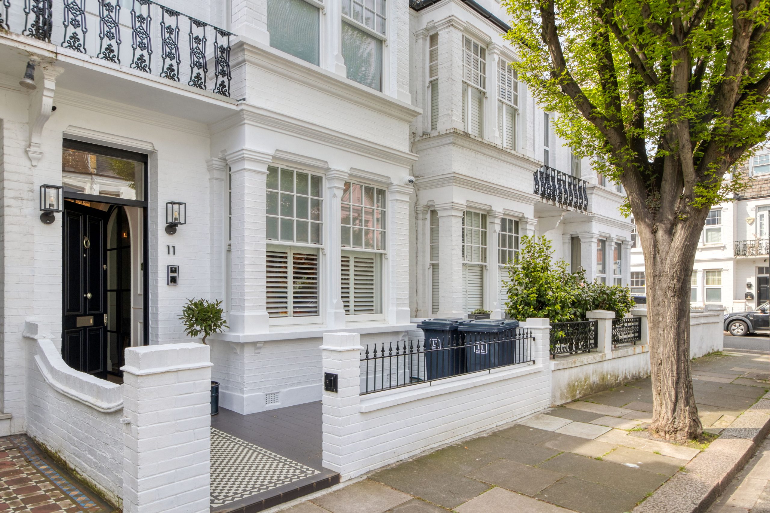 Exterior view of a refurbished residential building with clean white brickwork, decorative iron balconies, and a tree-lined street.