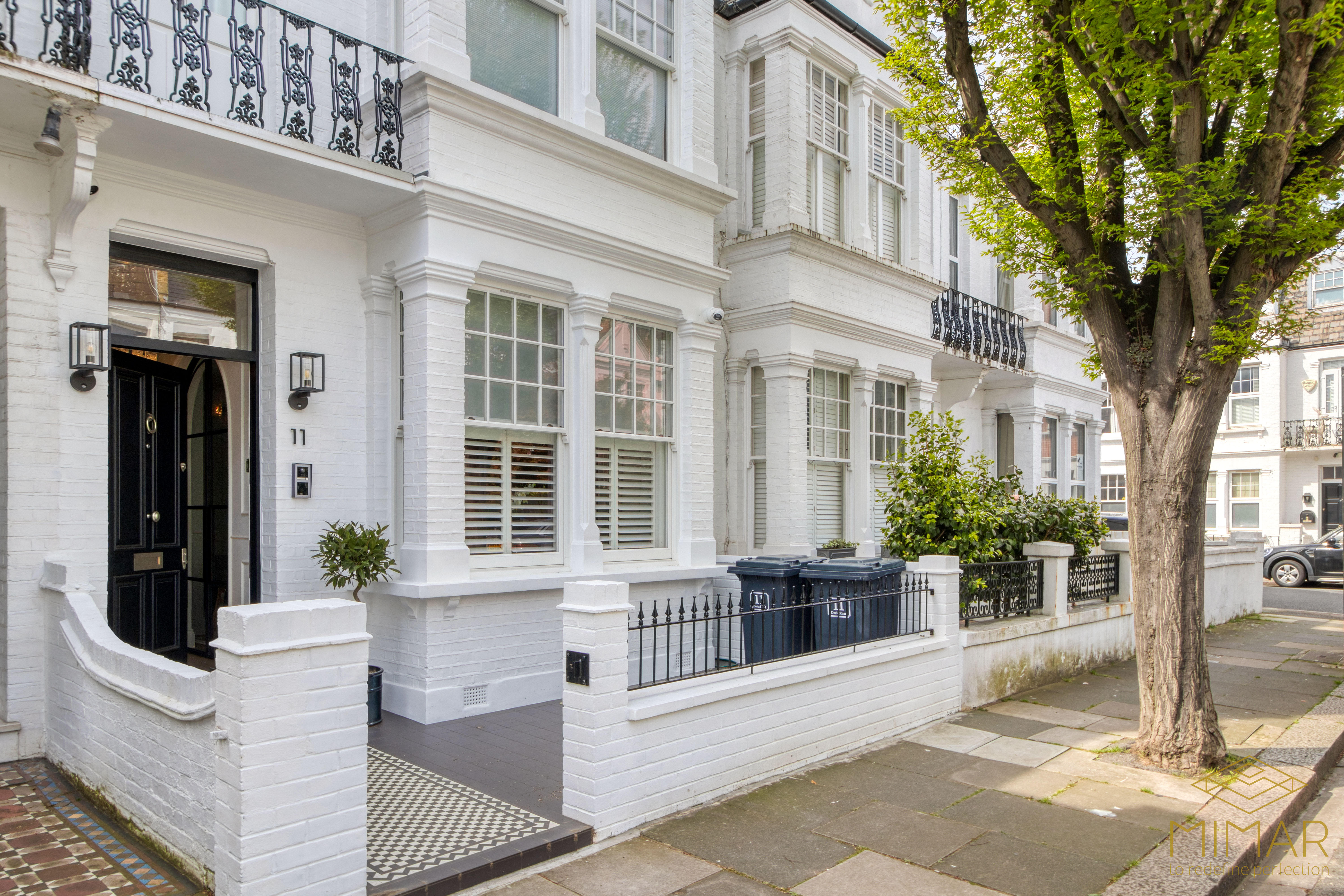 A street view of a refurbished white brick residential building with decorative railings, modern windows, and a tiled entrance walkway.