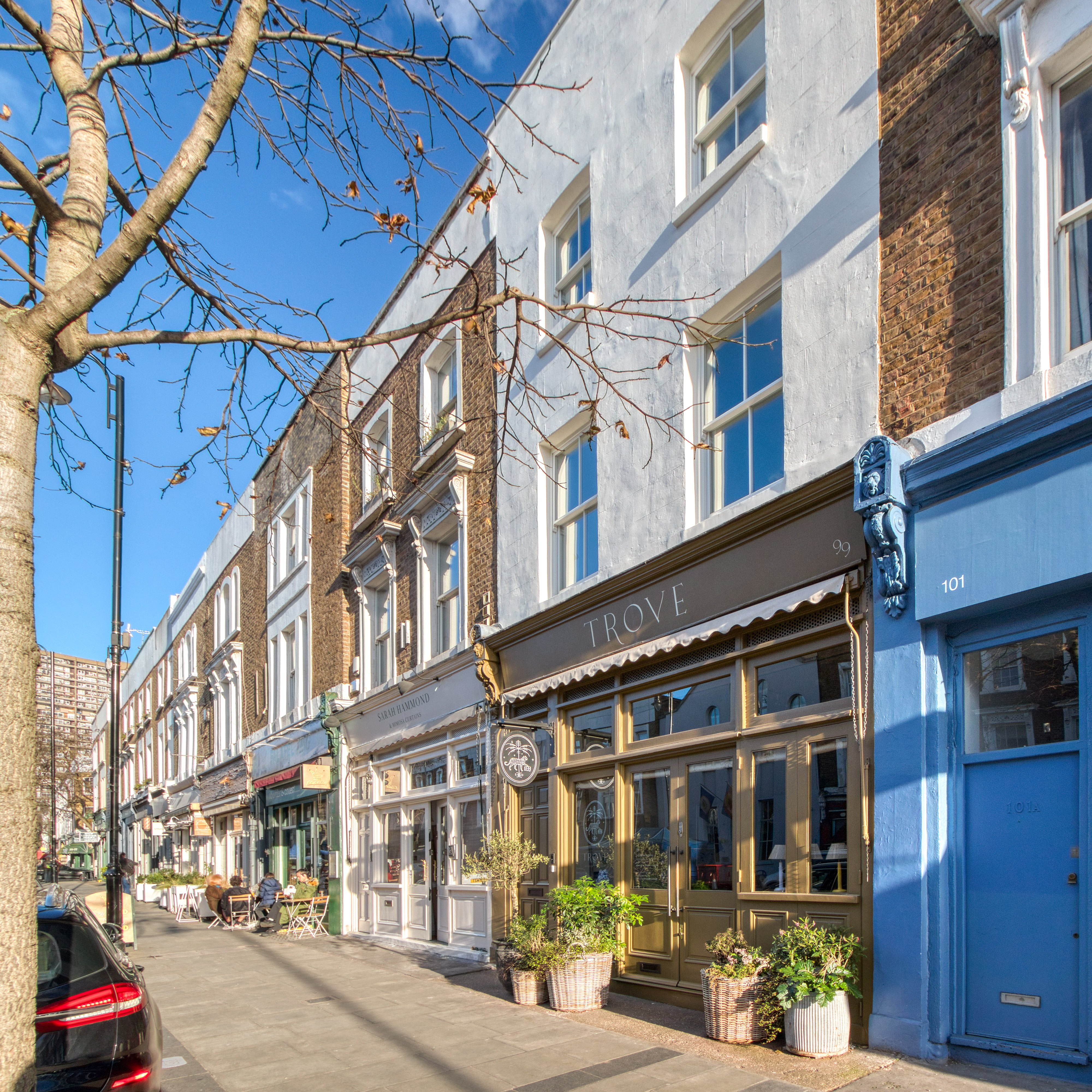 Row of refurbished townhouses with shops on the ground floor, featuring updated facades and large windows.