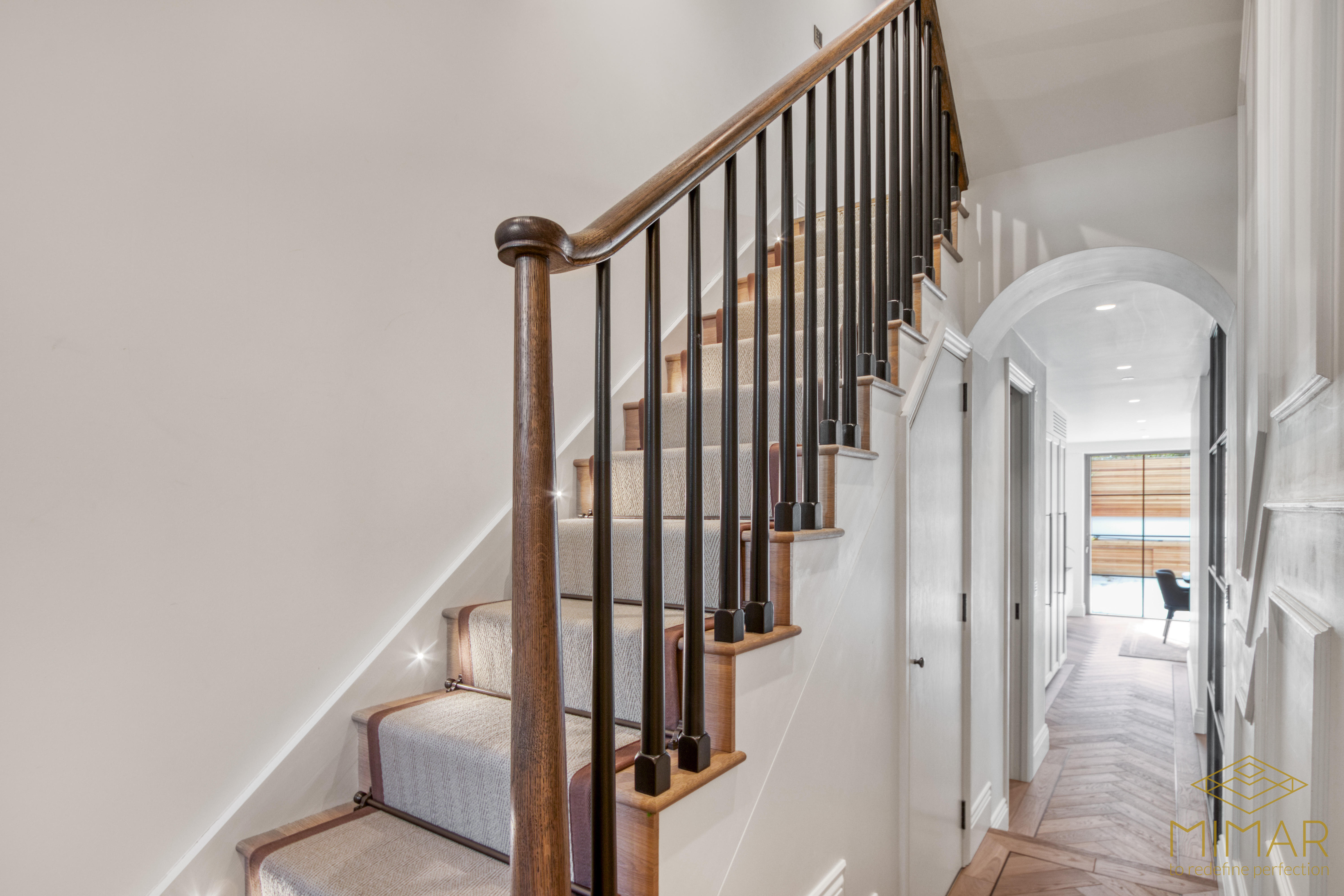 A modern residential staircase with wooden handrails and carpeted steps in a newly refurbished hallway.