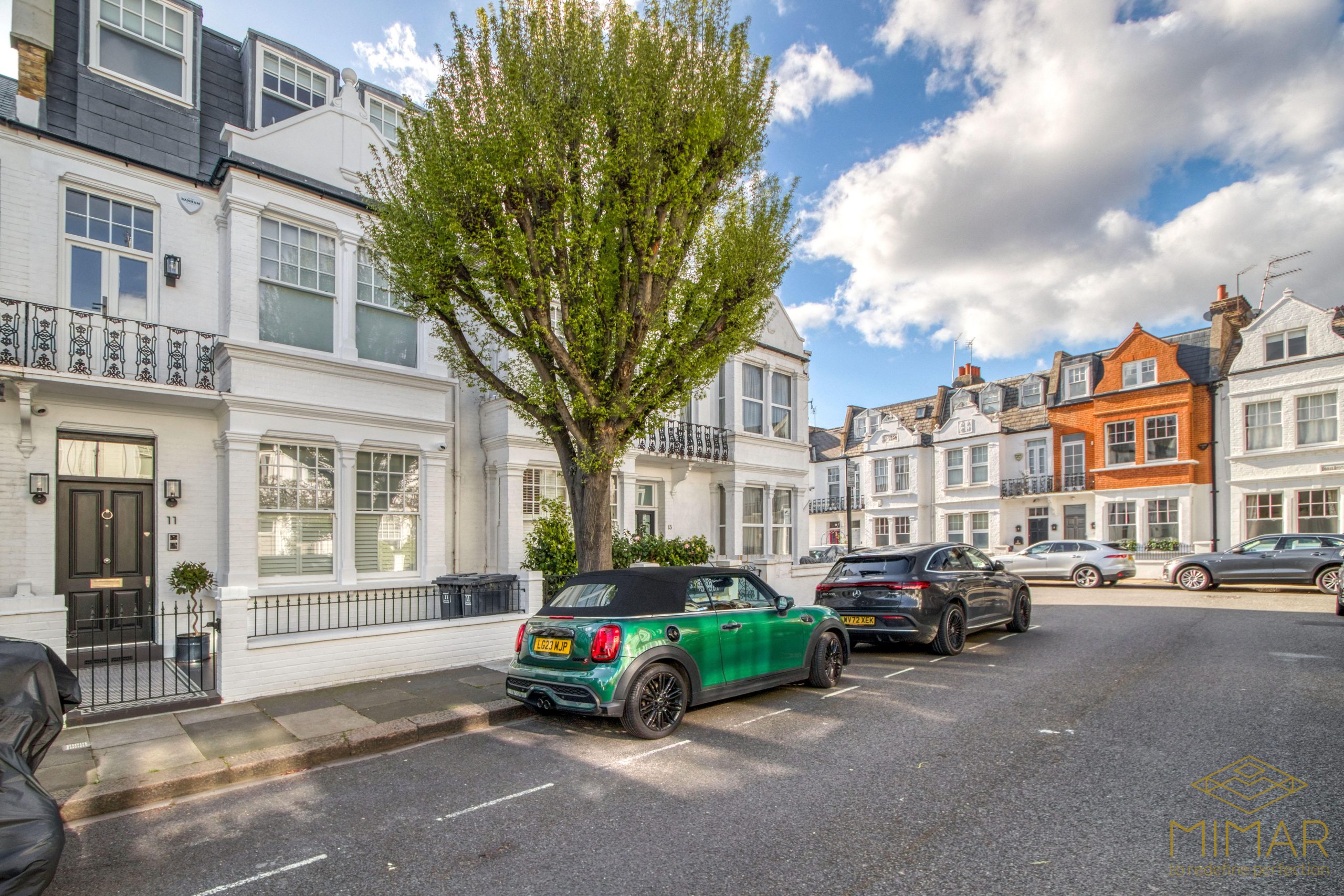 A street view of a row of stylish townhouses with vehicles parked along the curb under a clear sky.