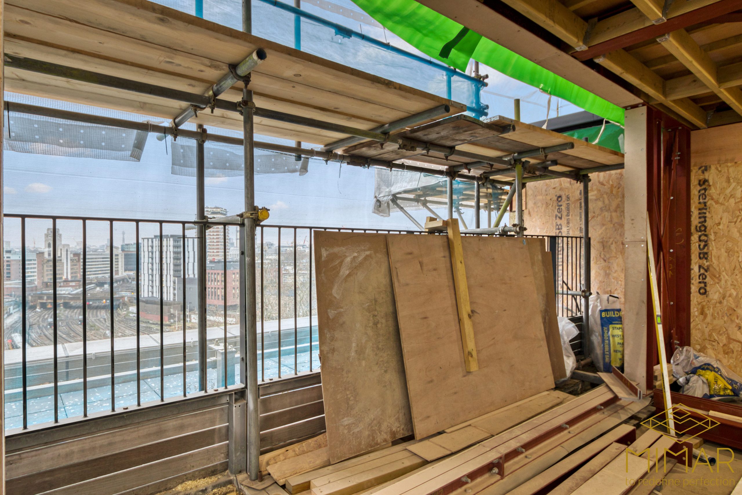 Scaffolding setup at a construction site with safety nets, building materials, and a view of the cityscape in the background.