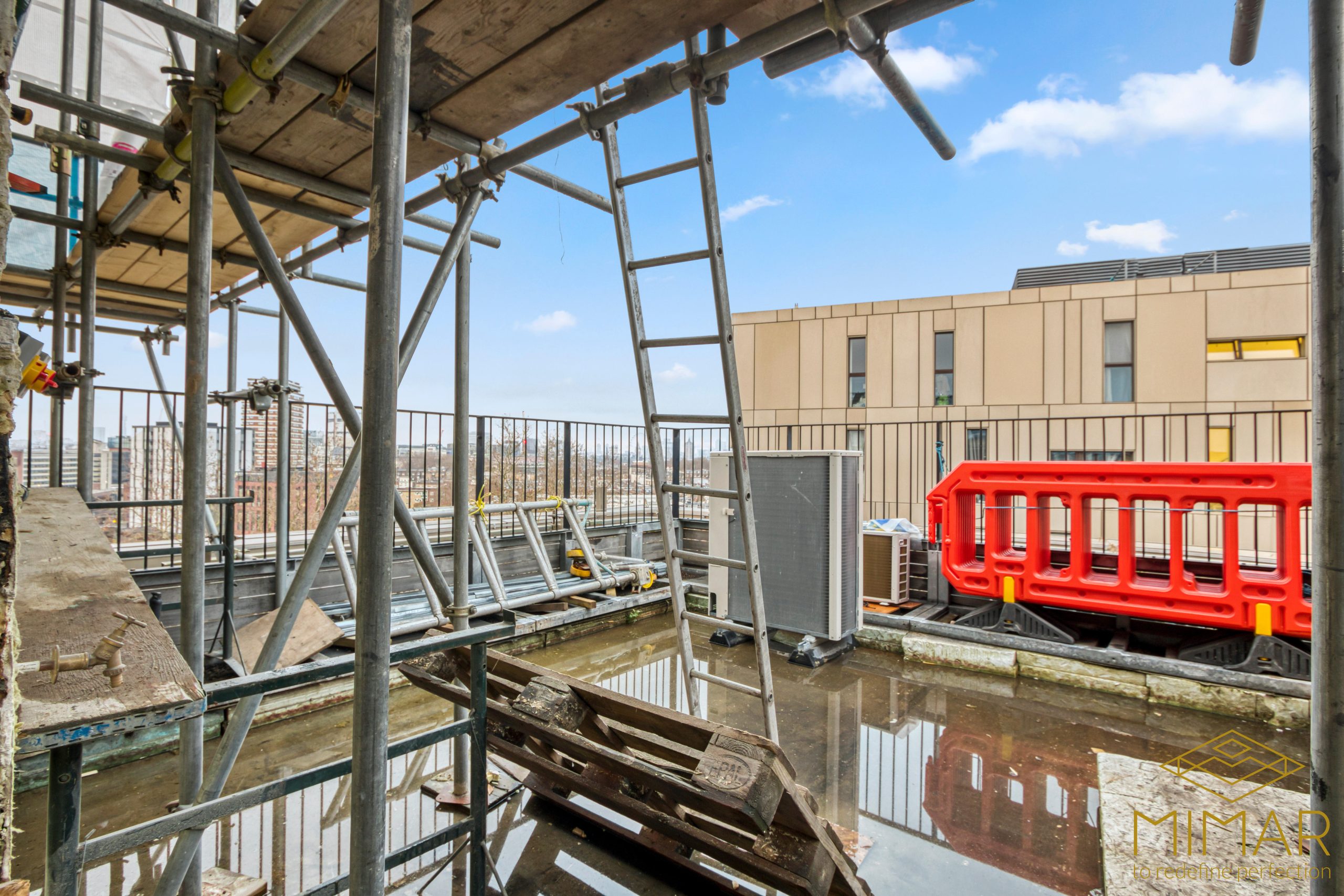 Scaffolding setup on a rooftop construction site with visible ladders, barriers, and building structures in the background.
