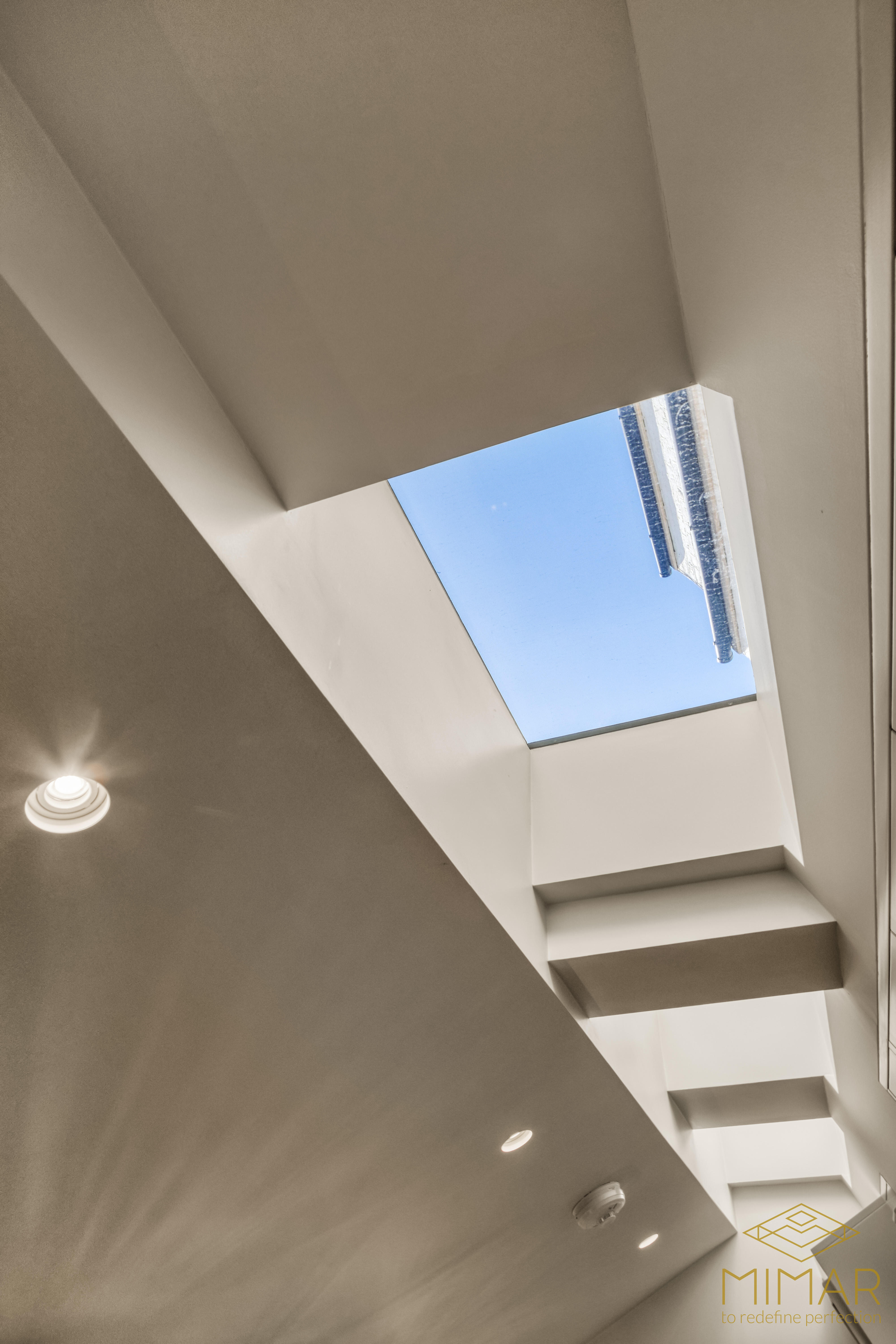 A modern ceiling with recessed lighting and a large skylight allowing natural light into the space.